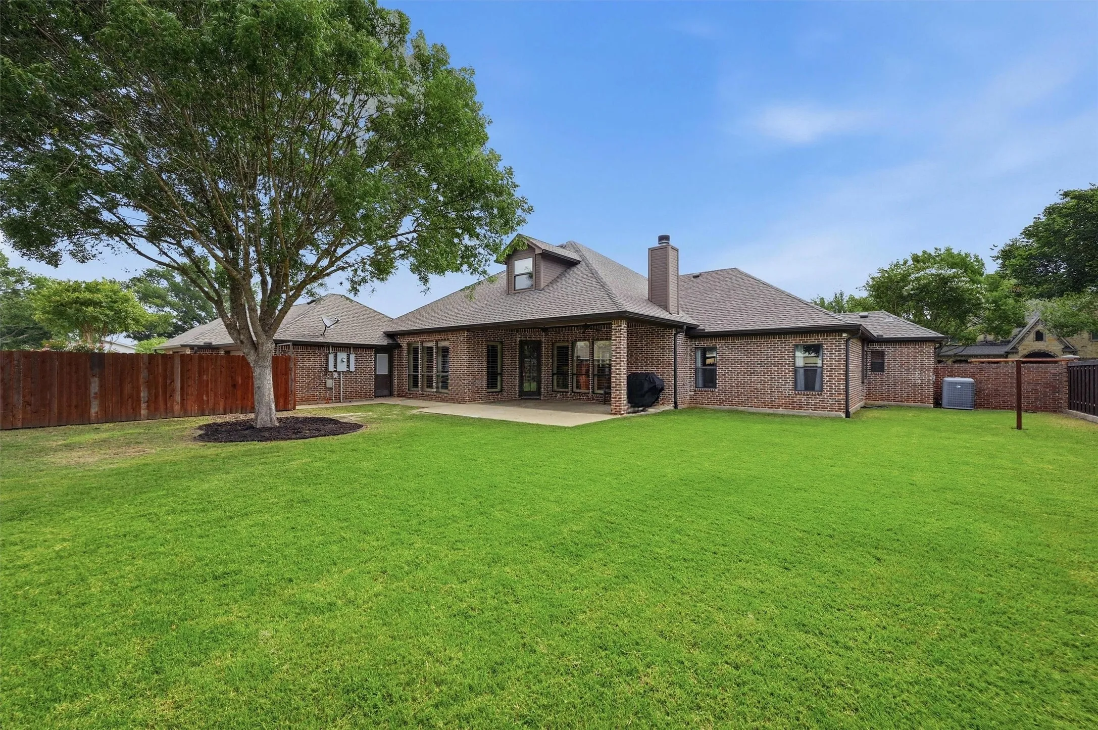 Expansive green lawn featuring a mature tree, a full brick exterior, and a covered patio
