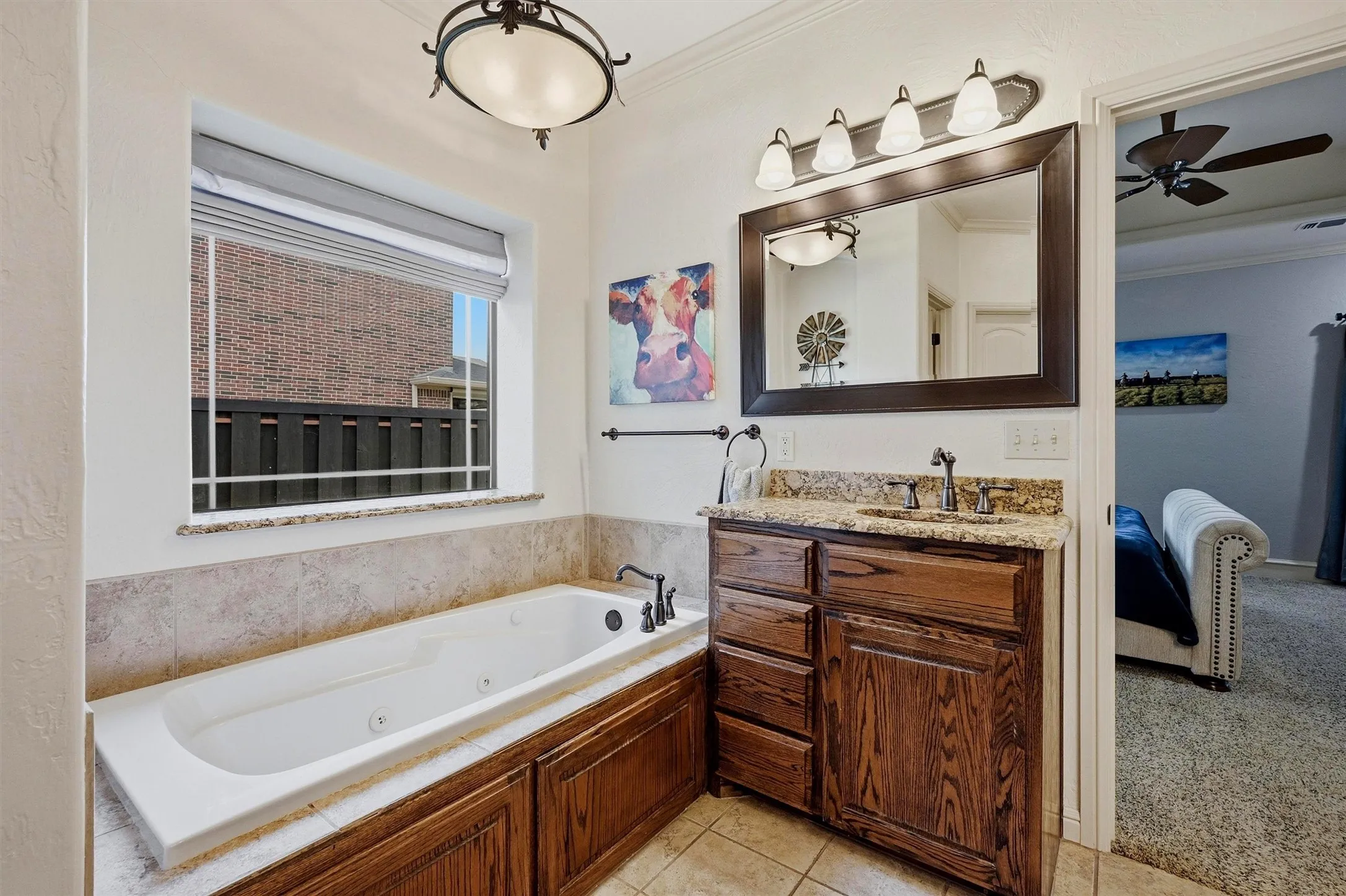 Bathroom featuring a built-in jetted tub with tile surround, a single vanity with stone countertop and wood cabinetry, and an ornate overhead light fixture