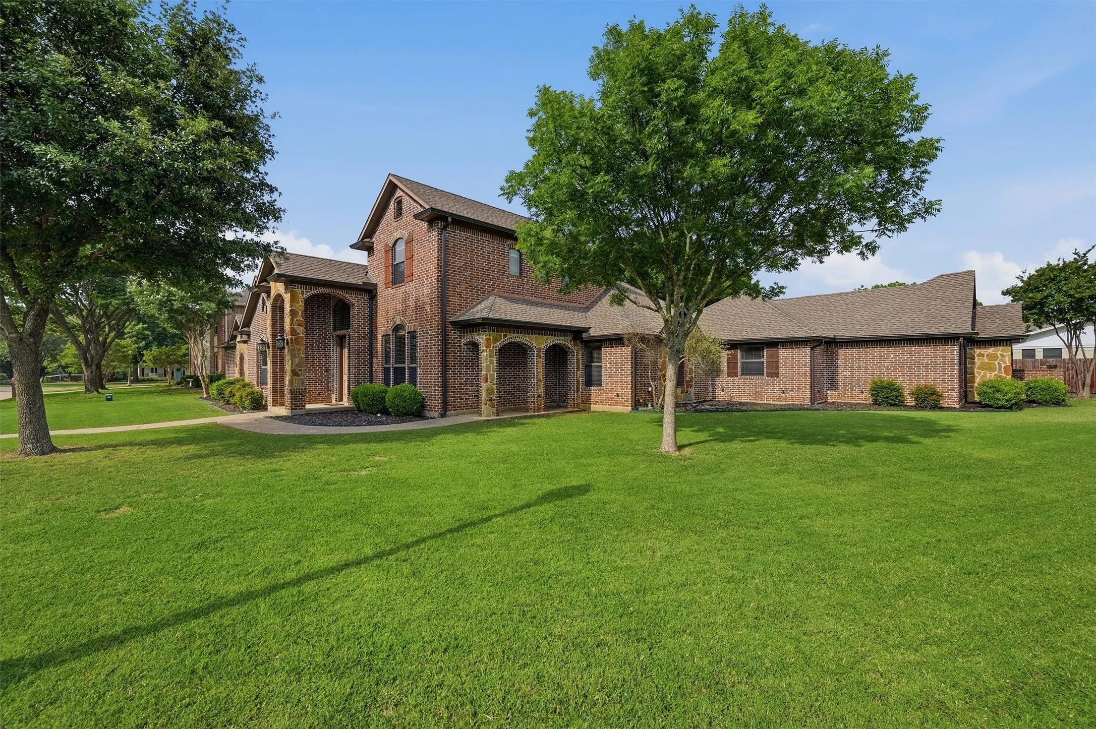 Brick facade residence featuring stone archways, multiple gables, and a shingle roof