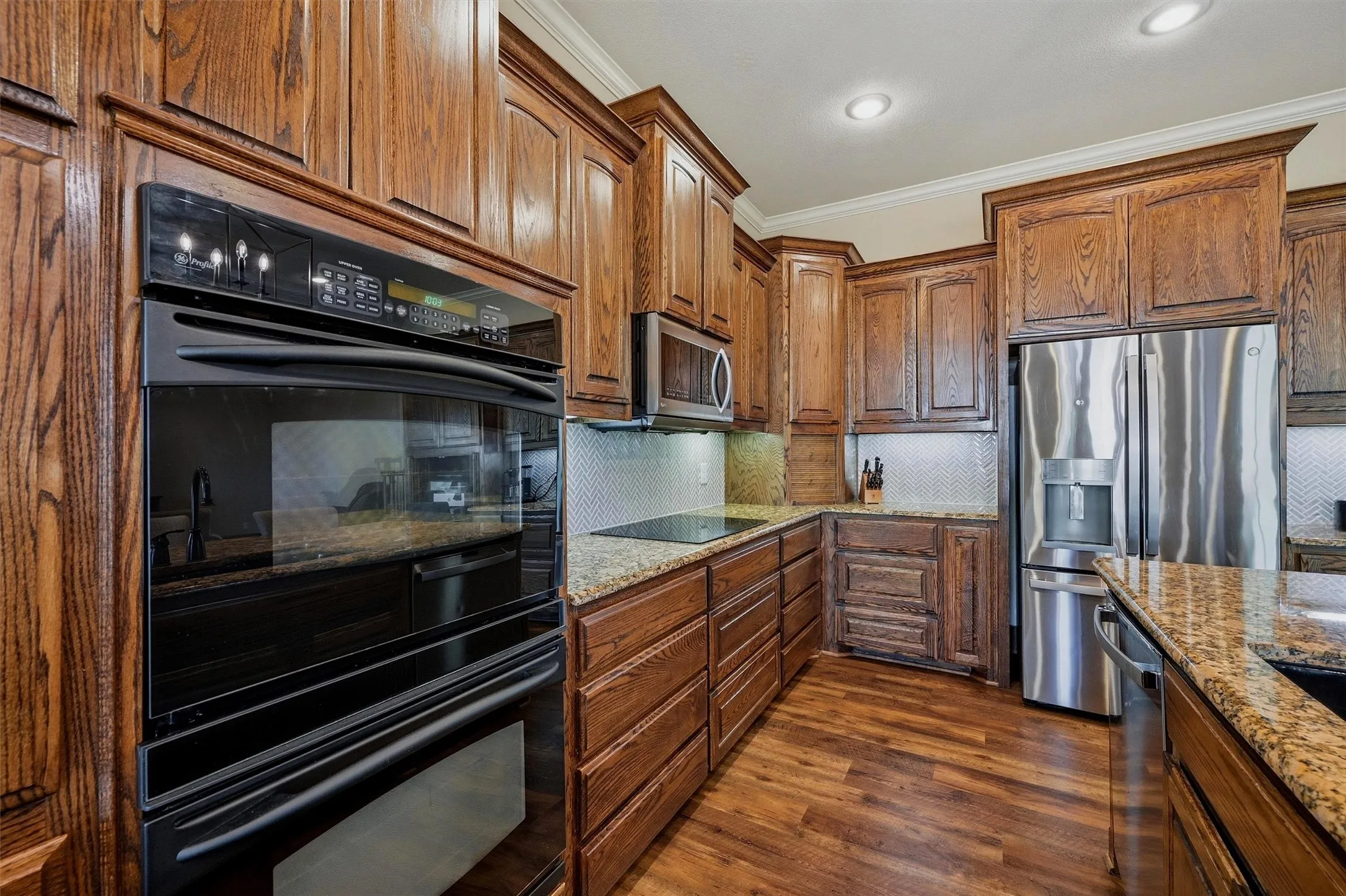 Kitchen featuring rich wood cabinetry, granite countertops, an integrated double oven, stainless steel French door refrigerator, and wood-finish flooring