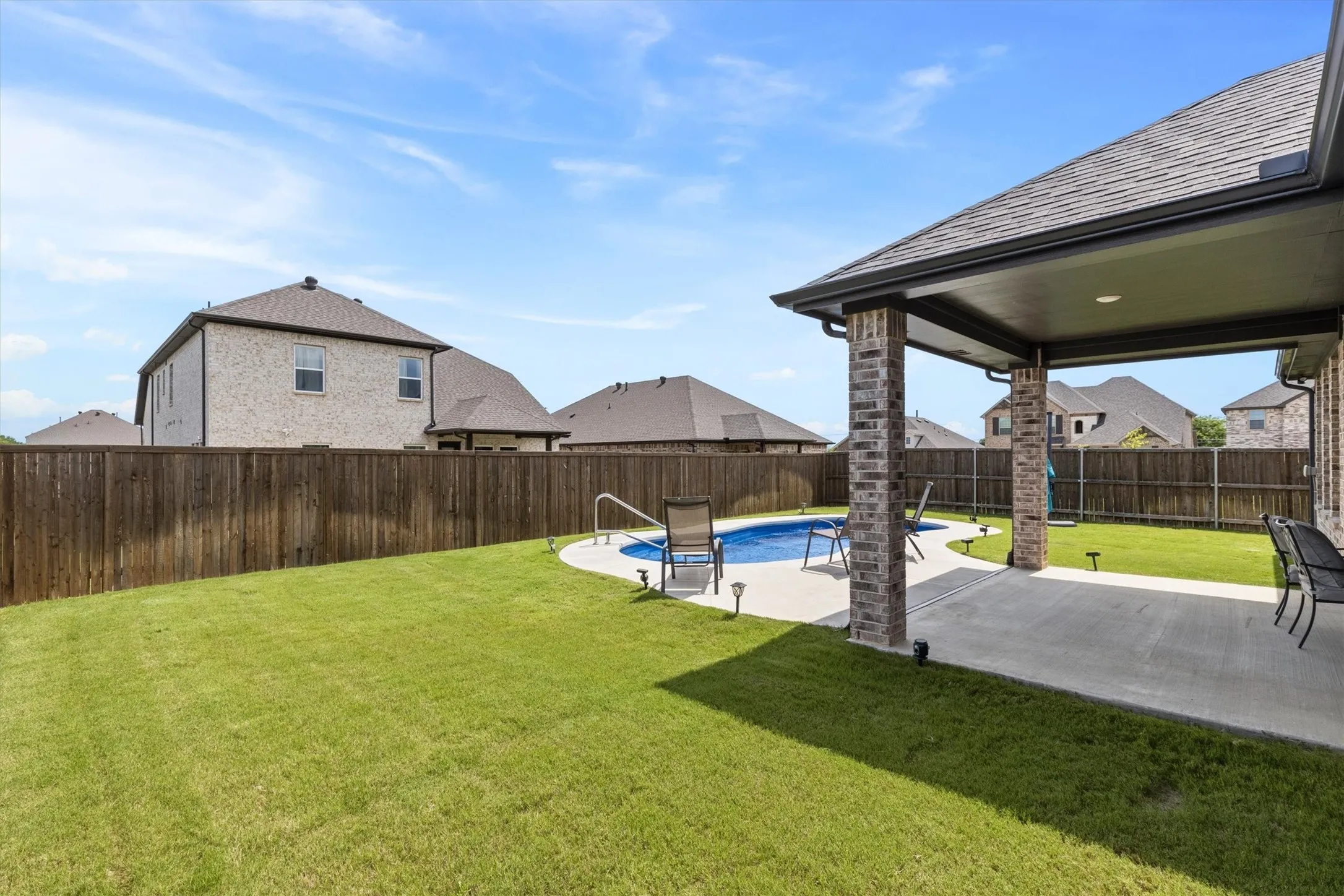 Private backyard featuring a fenced perimeter, a curved swimming pool, and a covered patio area with brick columns