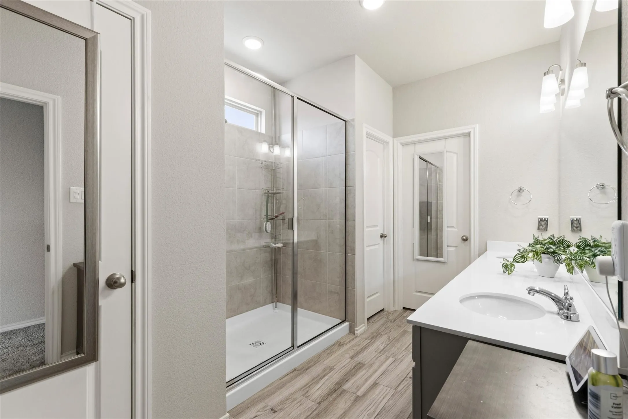Bathroom featuring a frameless glass shower enclosure, wood-finish flooring, a double vanity with undermount sinks, and a quartz countertop