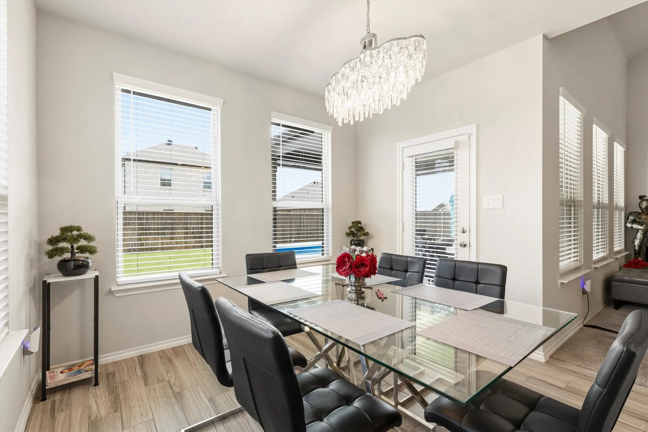 Dining area featuring wood-finish tile flooring, multiple large windows with blinds, a crystal chandelier, and a glass-top dining table