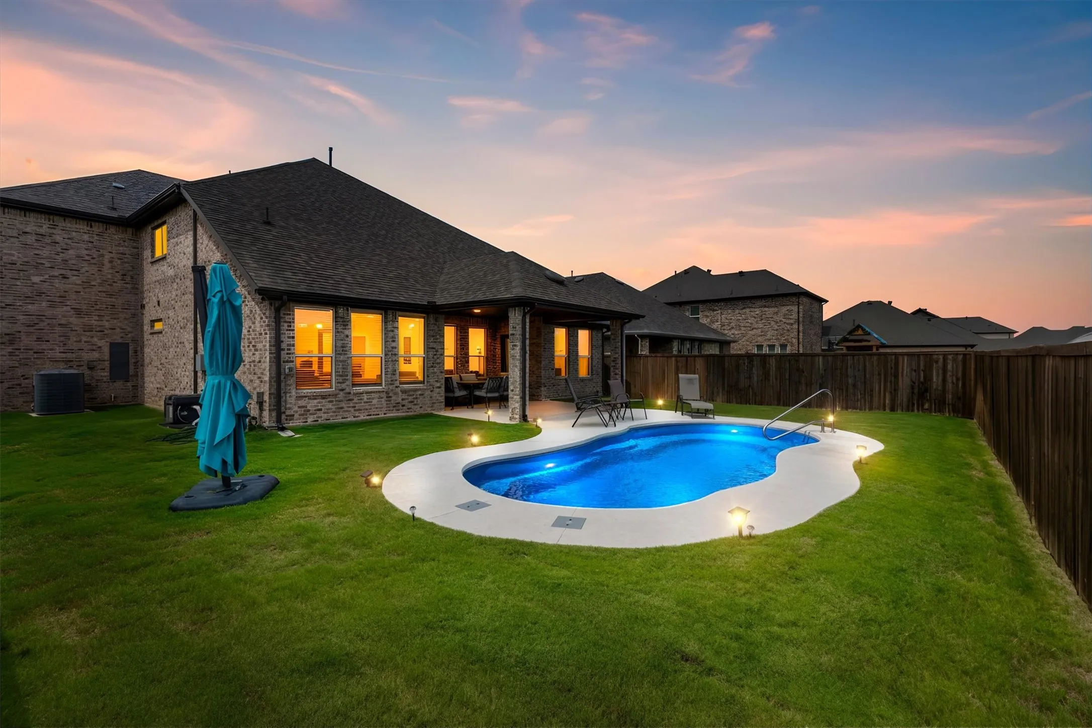 Brick exterior residence featuring a freeform swimming pool with integrated lighting, a concrete pool deck, and perimeter ground lighting