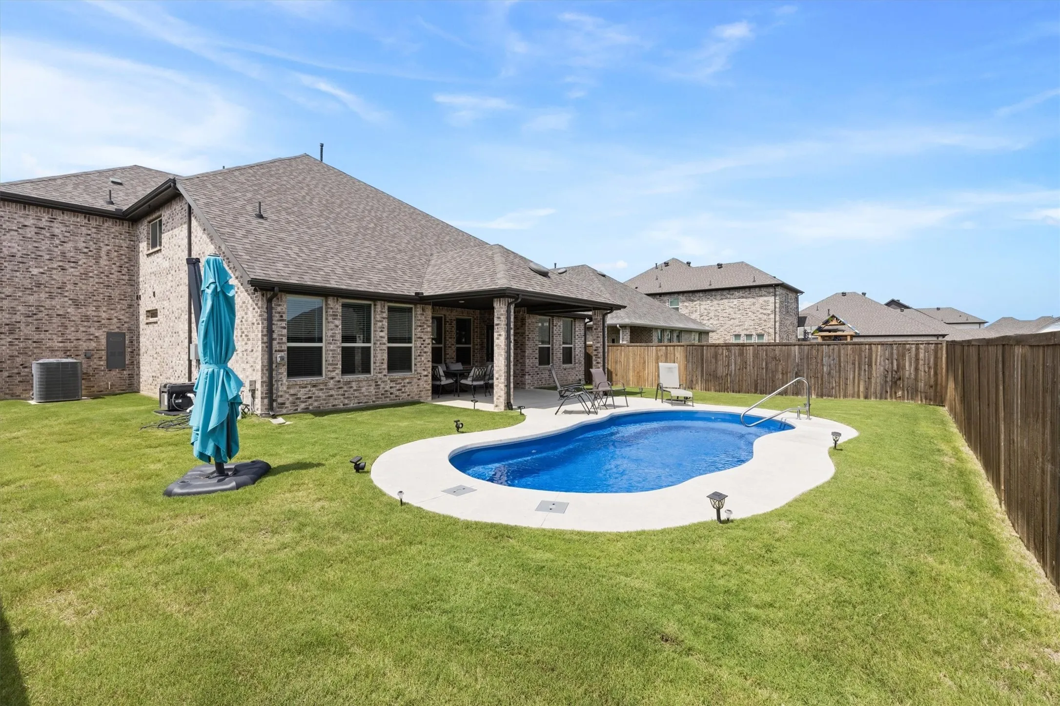 Backyard featuring an in-ground swimming pool with a concrete surround, an extended covered patio, and a private wooden fence