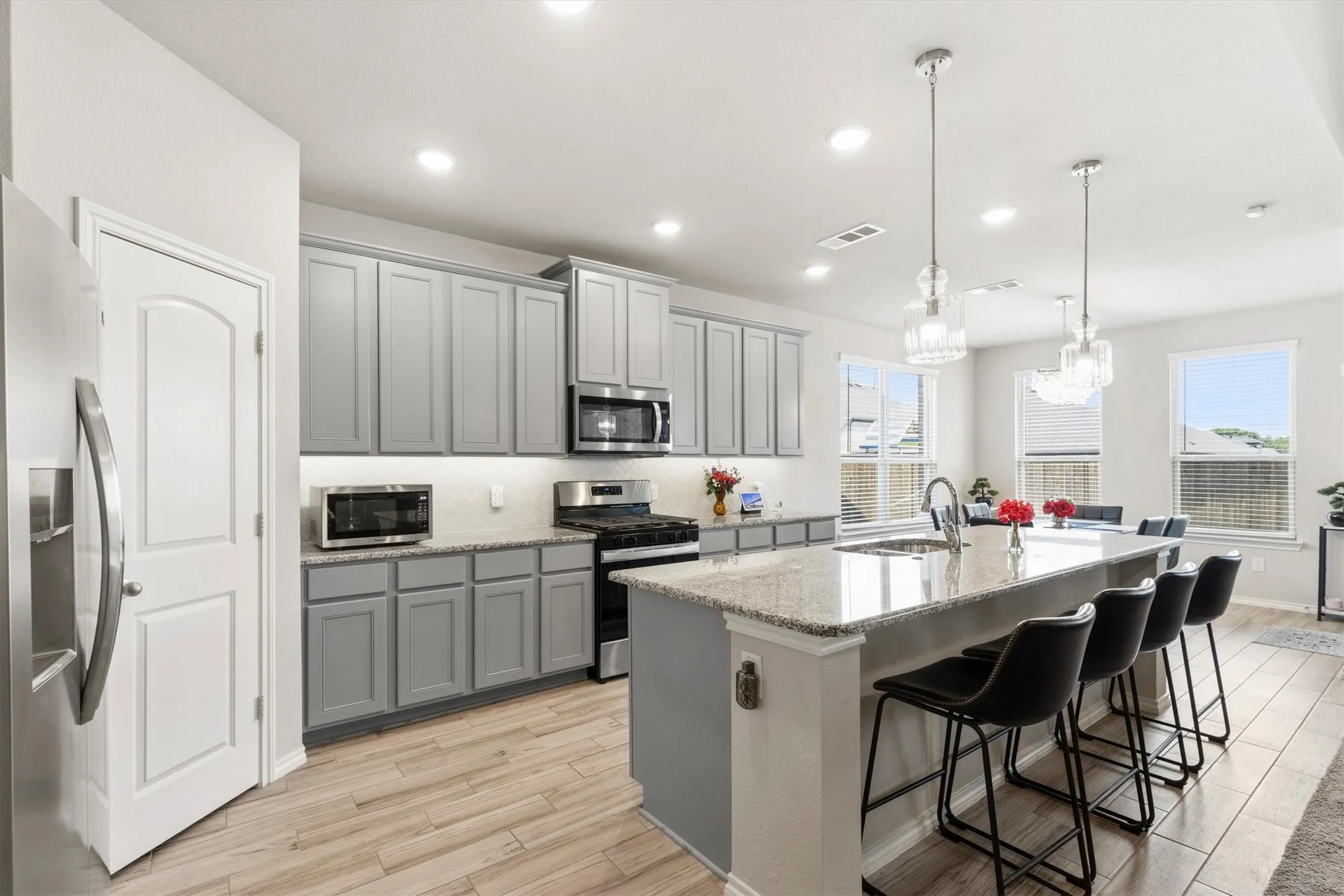 Modern kitchen featuring light gray cabinetry, wood-finish flooring, a large island with a composite countertop, recessed lighting, and pendant fixtures