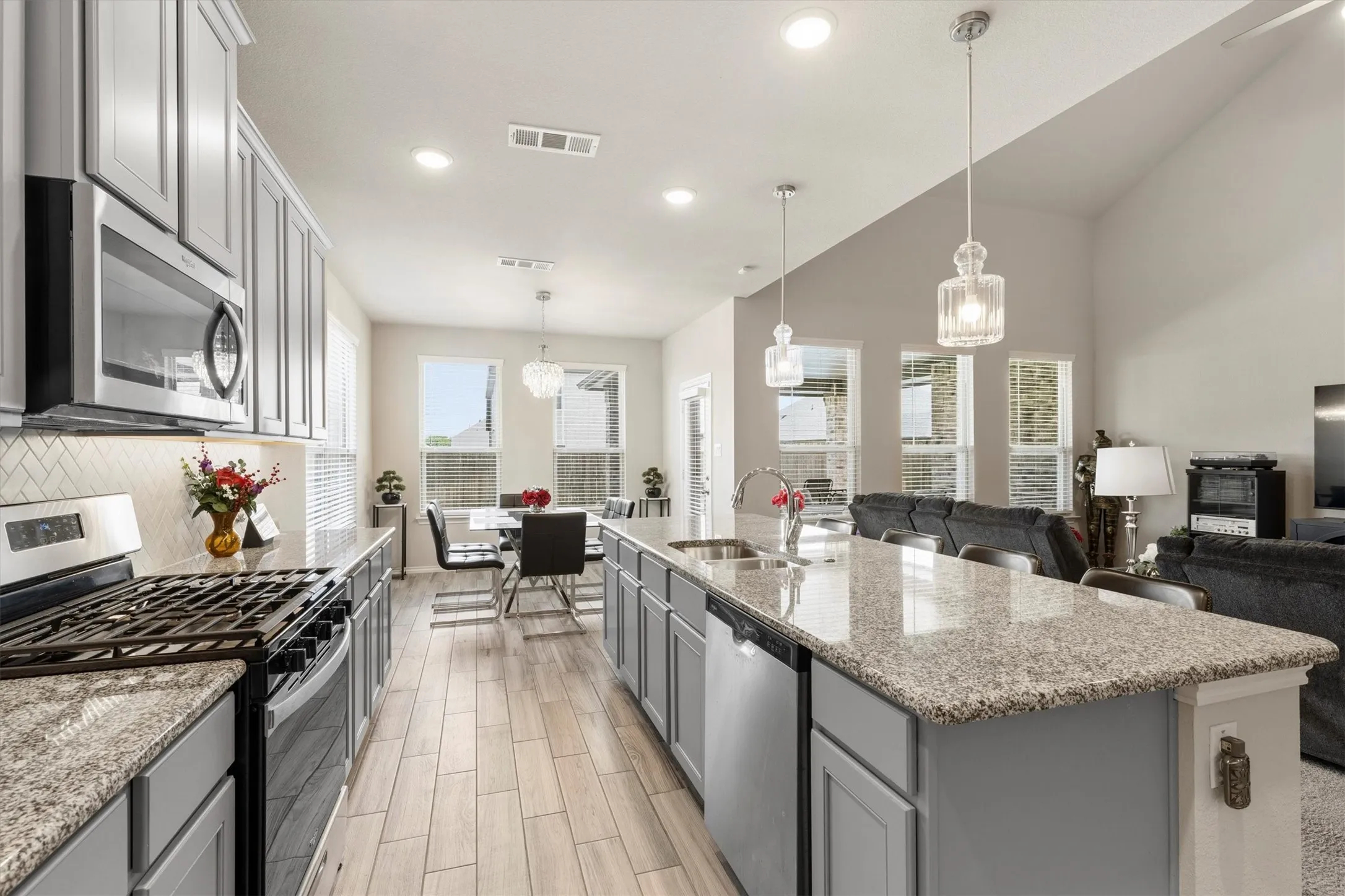 Modern kitchen featuring light gray cabinetry, stainless steel appliances, speckled stone countertops, and a subway tile backsplash