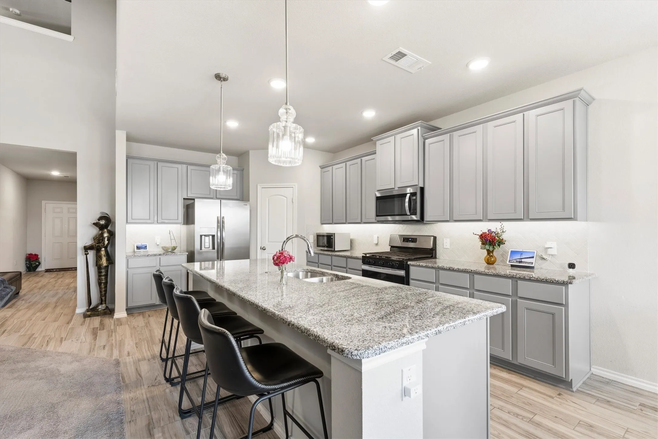 Kitchen featuring an expansive island with a double basin sink and integrated seating, light gray cabinetry, stainless steel appliances, and recessed lighting