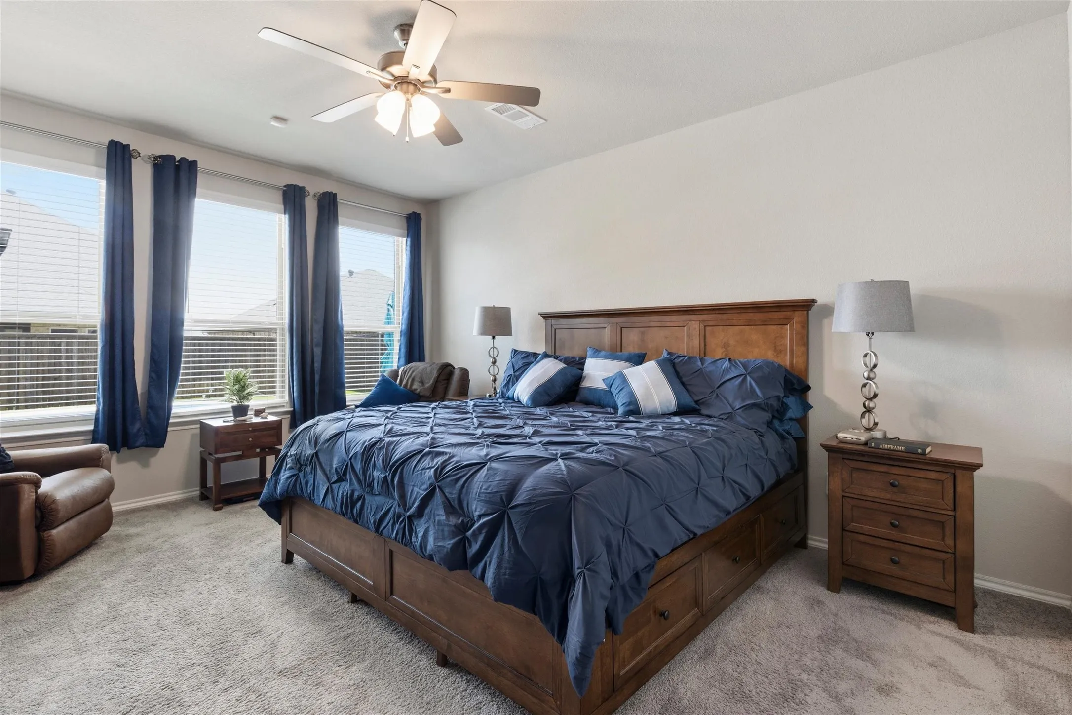 Carpeted bedroom featuring a ceiling fan, three windows with blinds, and neutral wall paint