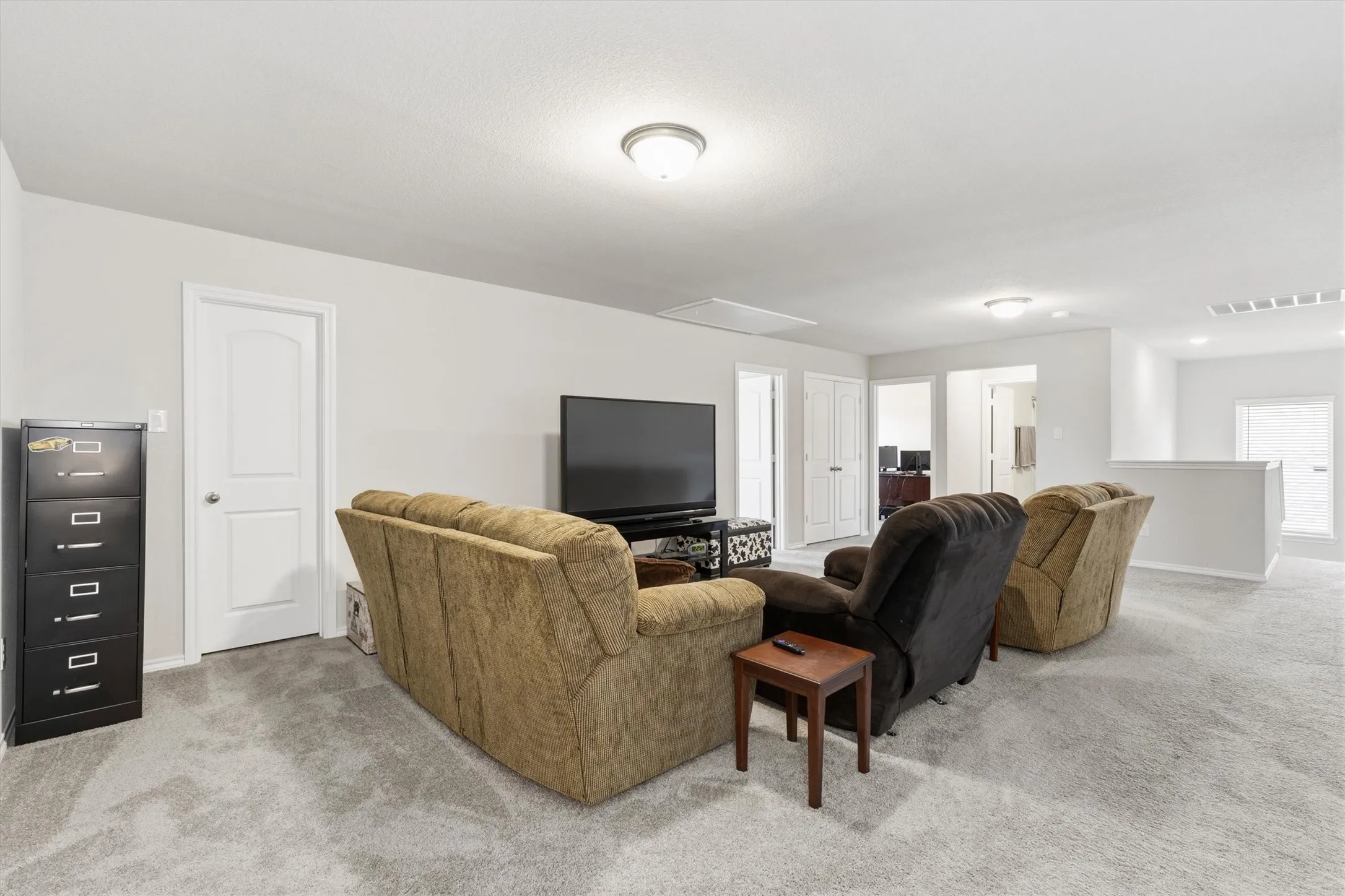Spacious carpeted room featuring light gray walls, multiple interior doors, and a partial low wall opening