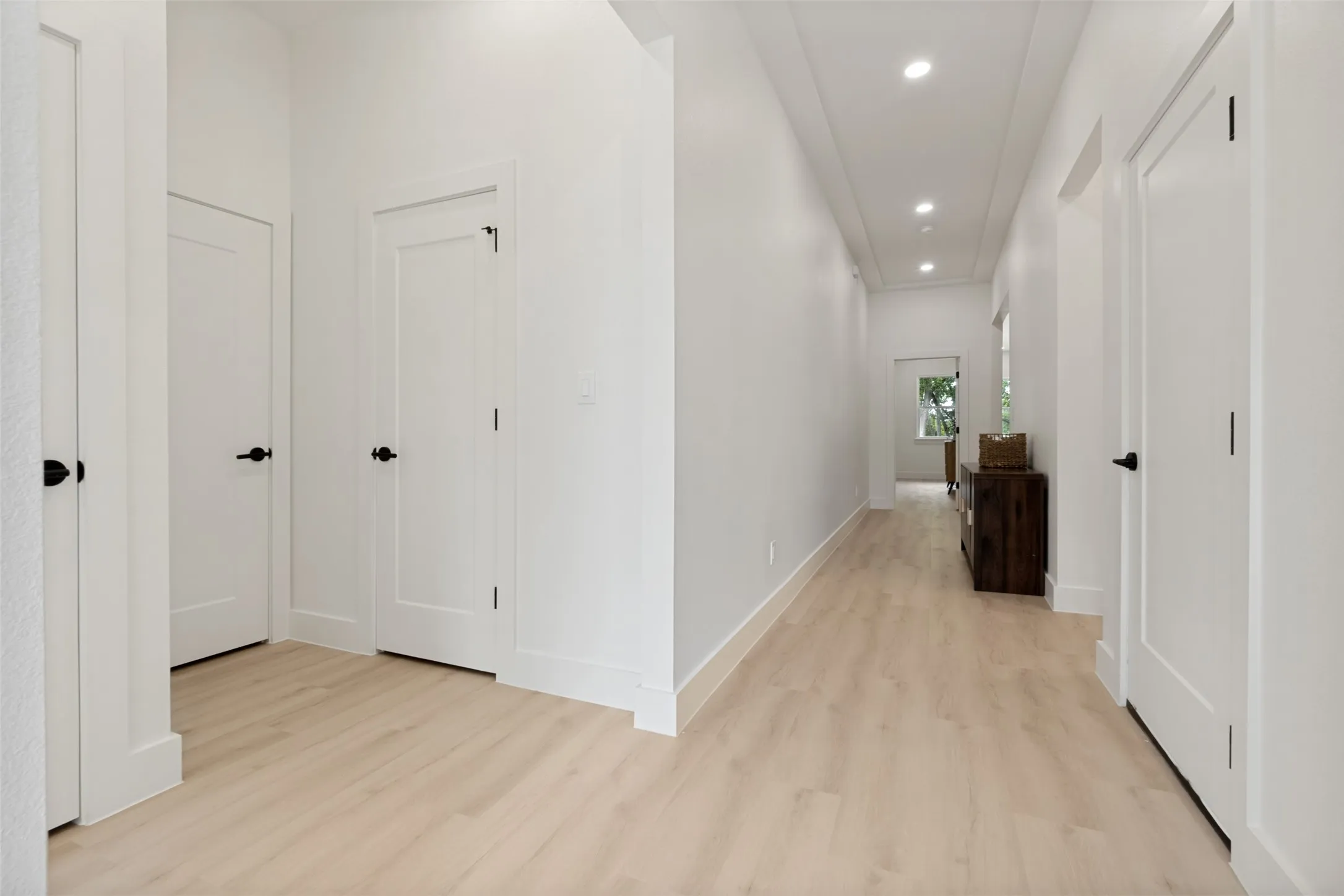 Bright hallway featuring light wood-finish flooring, recessed lighting, white walls, and contemporary panel doors with matte black hardware
