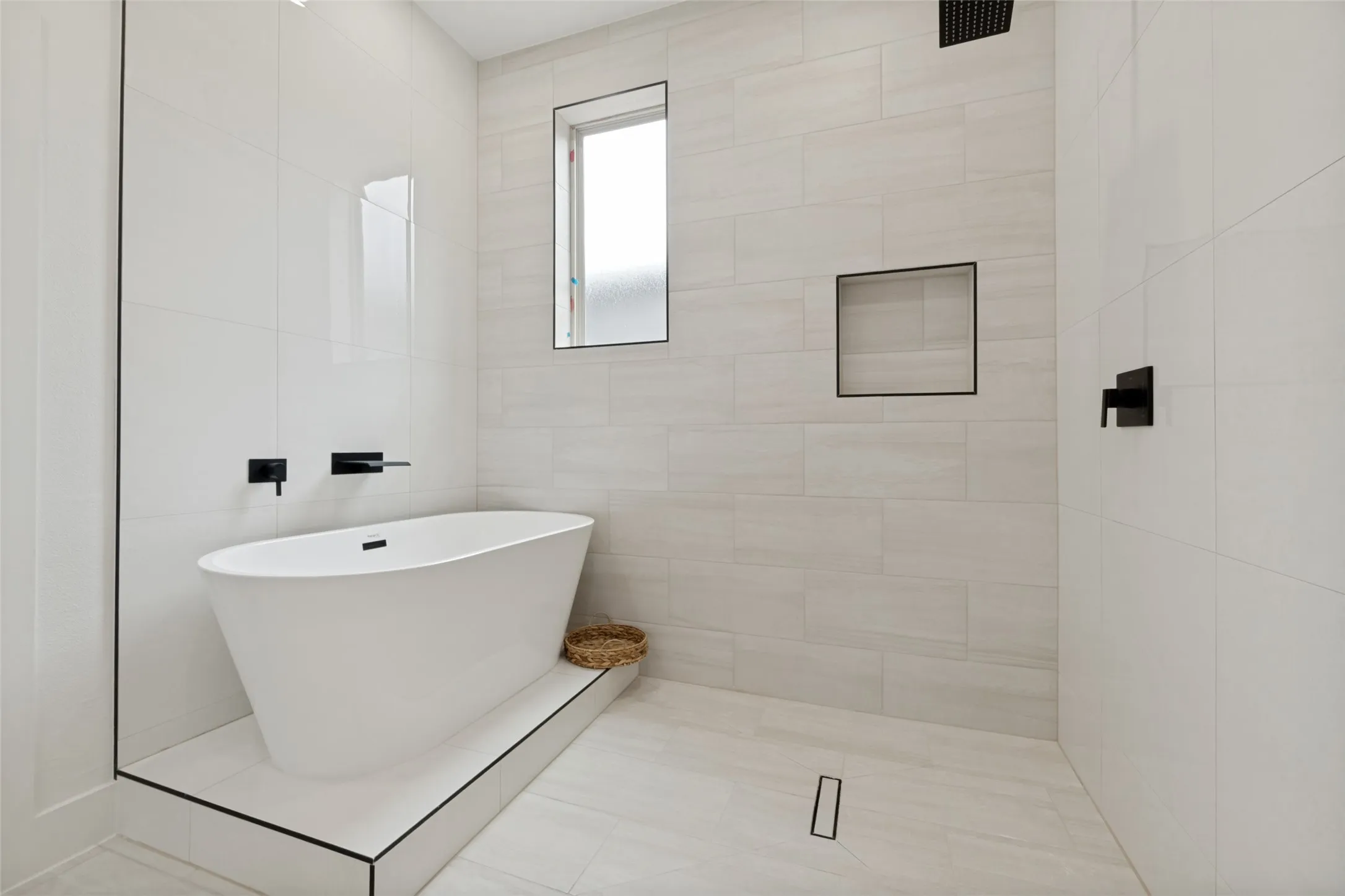 Modern bathroom featuring a freestanding soaking tub on a tiled platform, a walk-in shower with a linear drain, and matte black fixtures