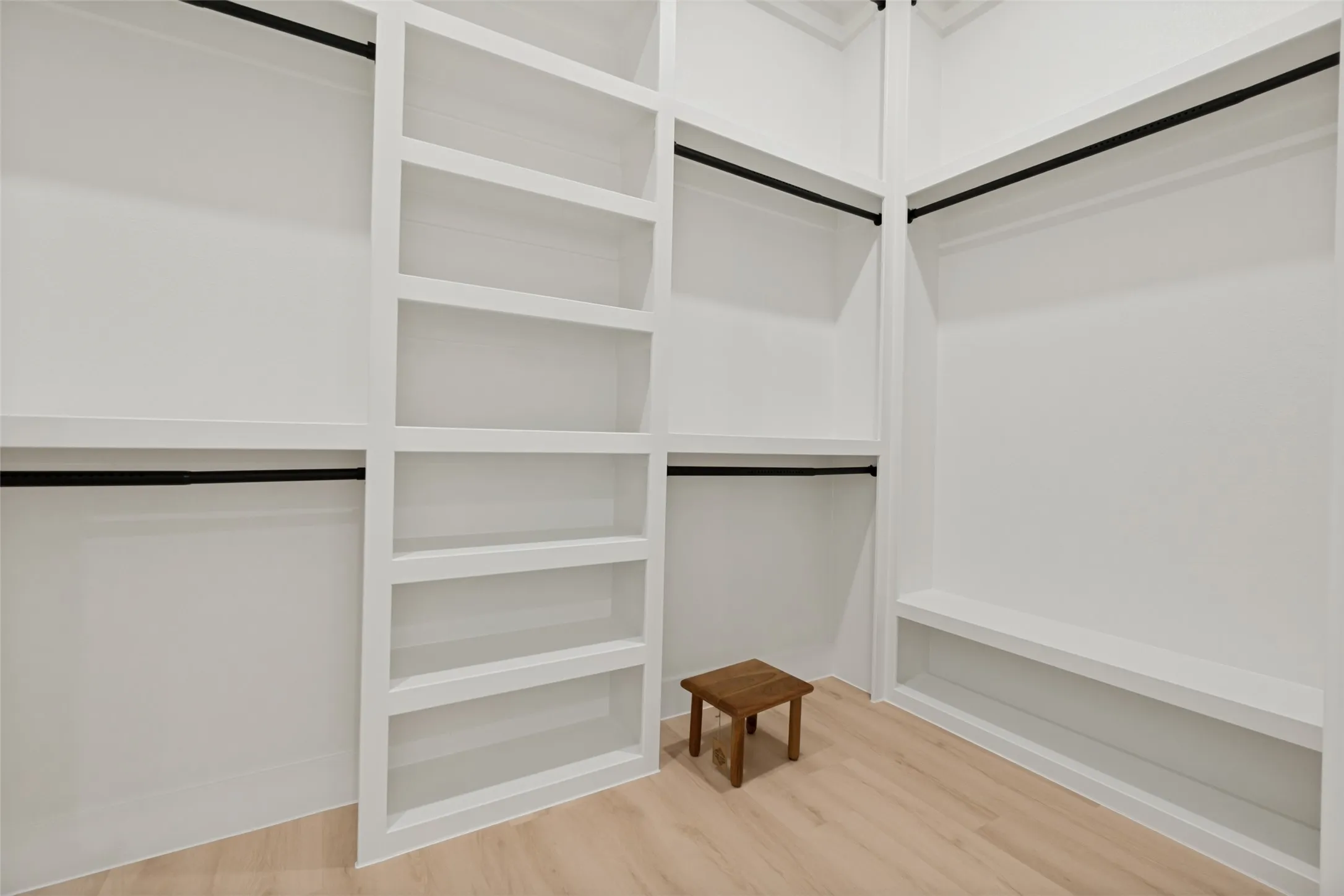 Custom closet system featuring light wood-finish flooring, built-in shelving, and multiple hanging rods with matte black finishes