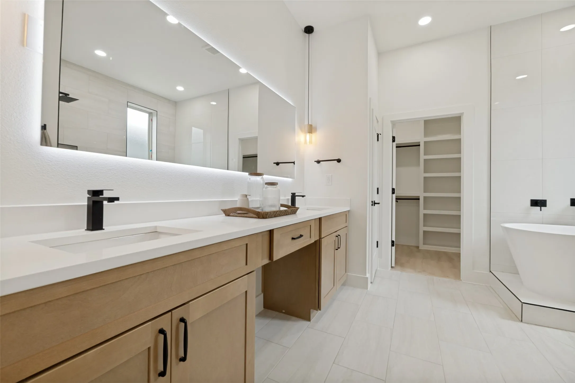 Contemporary bathroom with a double vanity featuring light wood-finish cabinetry, integrated sinks, and matte black fixtures