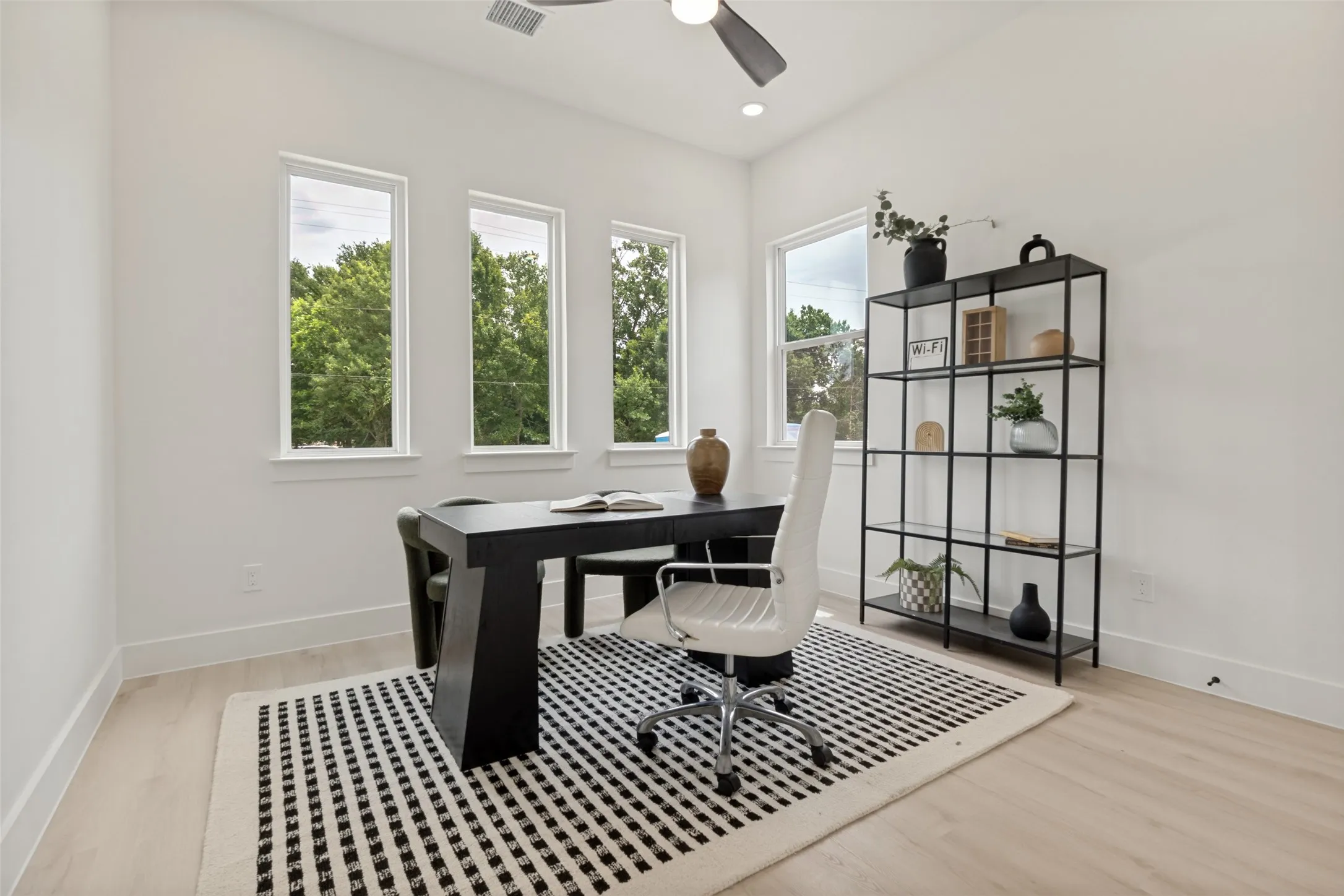Bright interior space featuring light wood-finish flooring, white walls, and a ceiling fan with integrated lighting