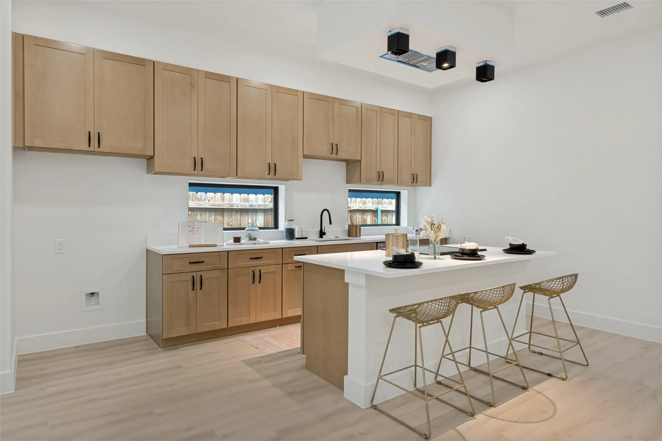 Contemporary kitchen featuring light wood-finish cabinetry, white countertops, and a central island with seating