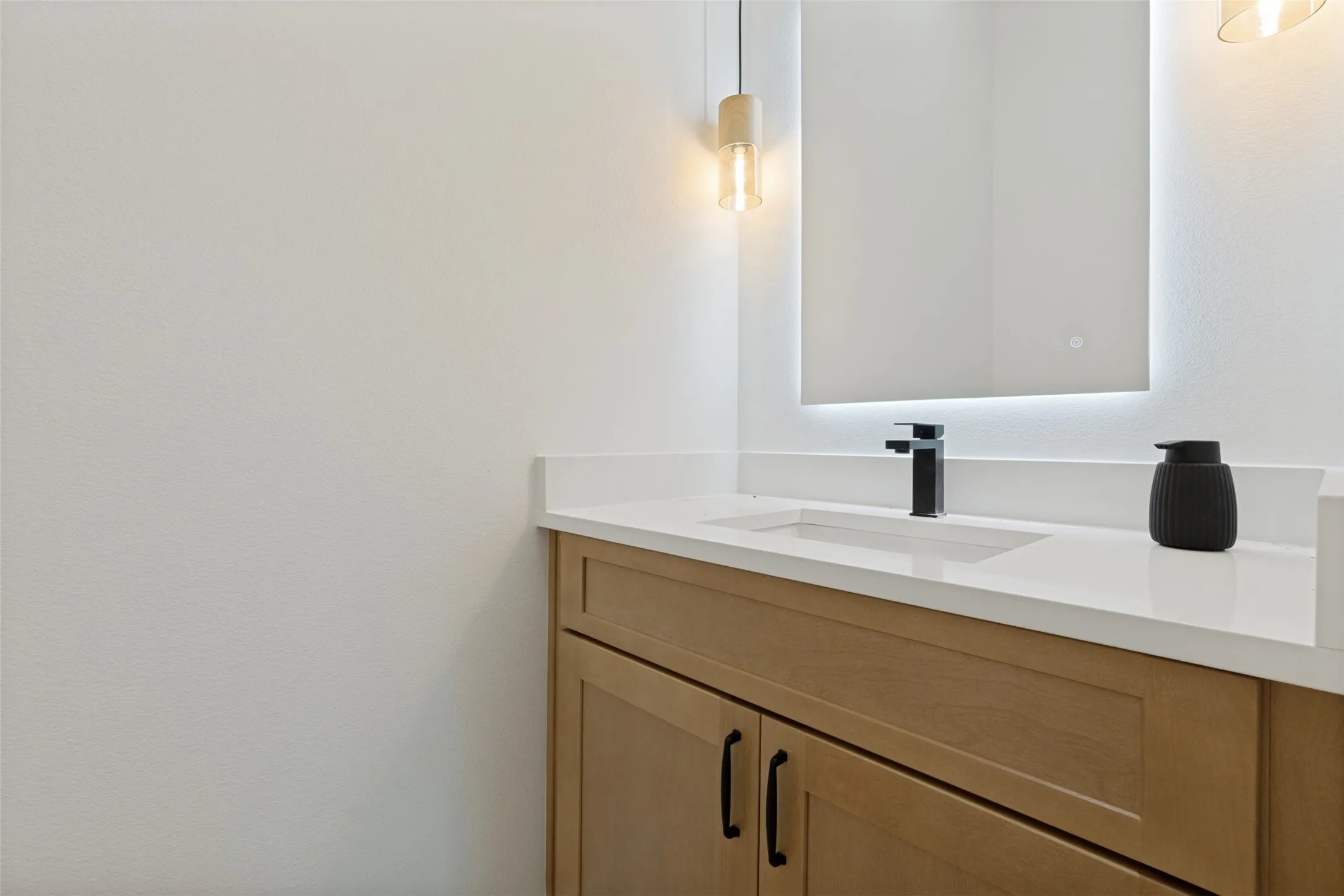 Modern vanity featuring a light wood-finish cabinet with matte black hardware, a pristine white countertop, and an undermount sink