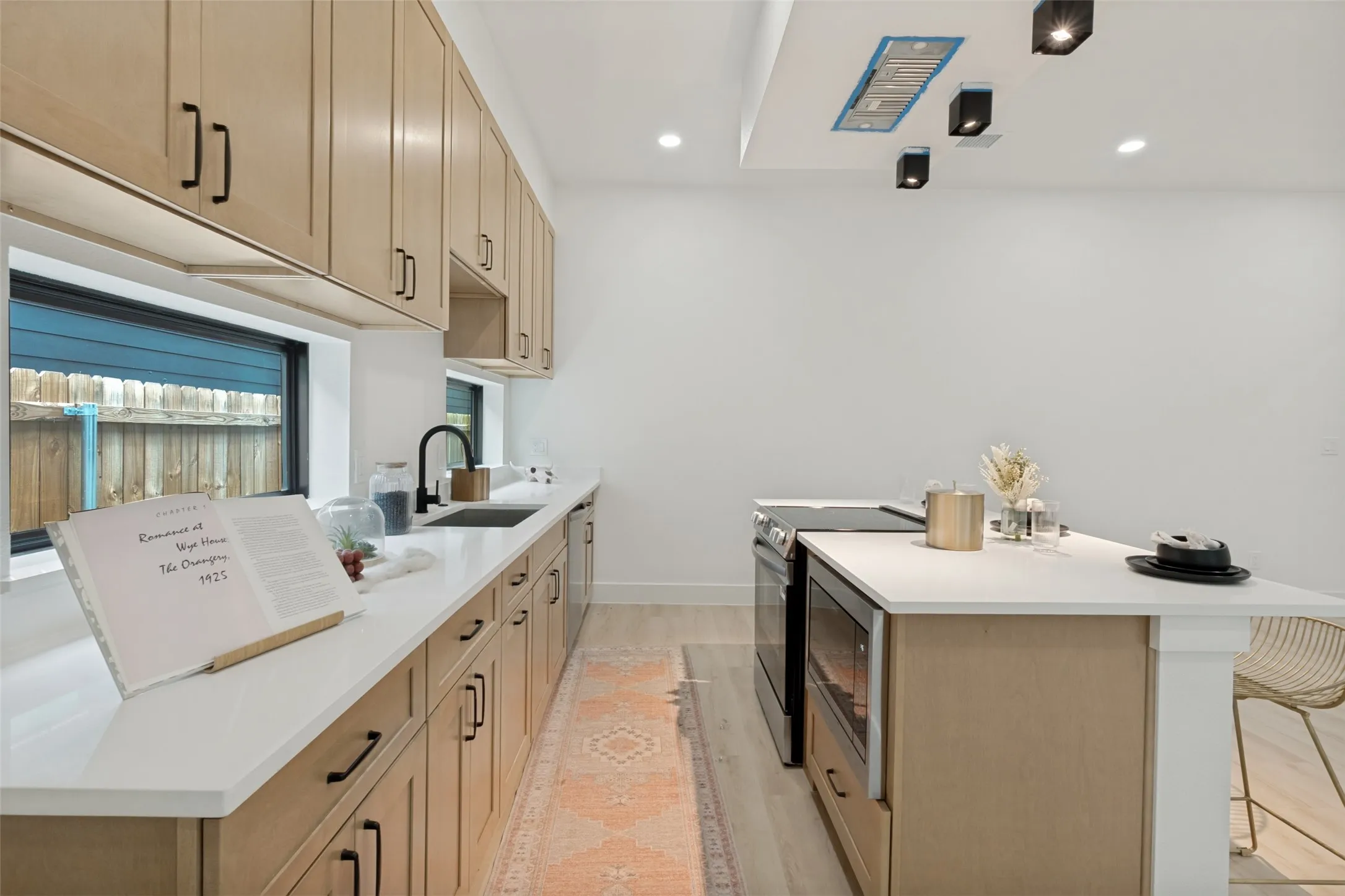Modern kitchen featuring light wood cabinetry with black hardware, white countertops, a black gooseneck faucet, an island with built-in appliances, and recessed lighting