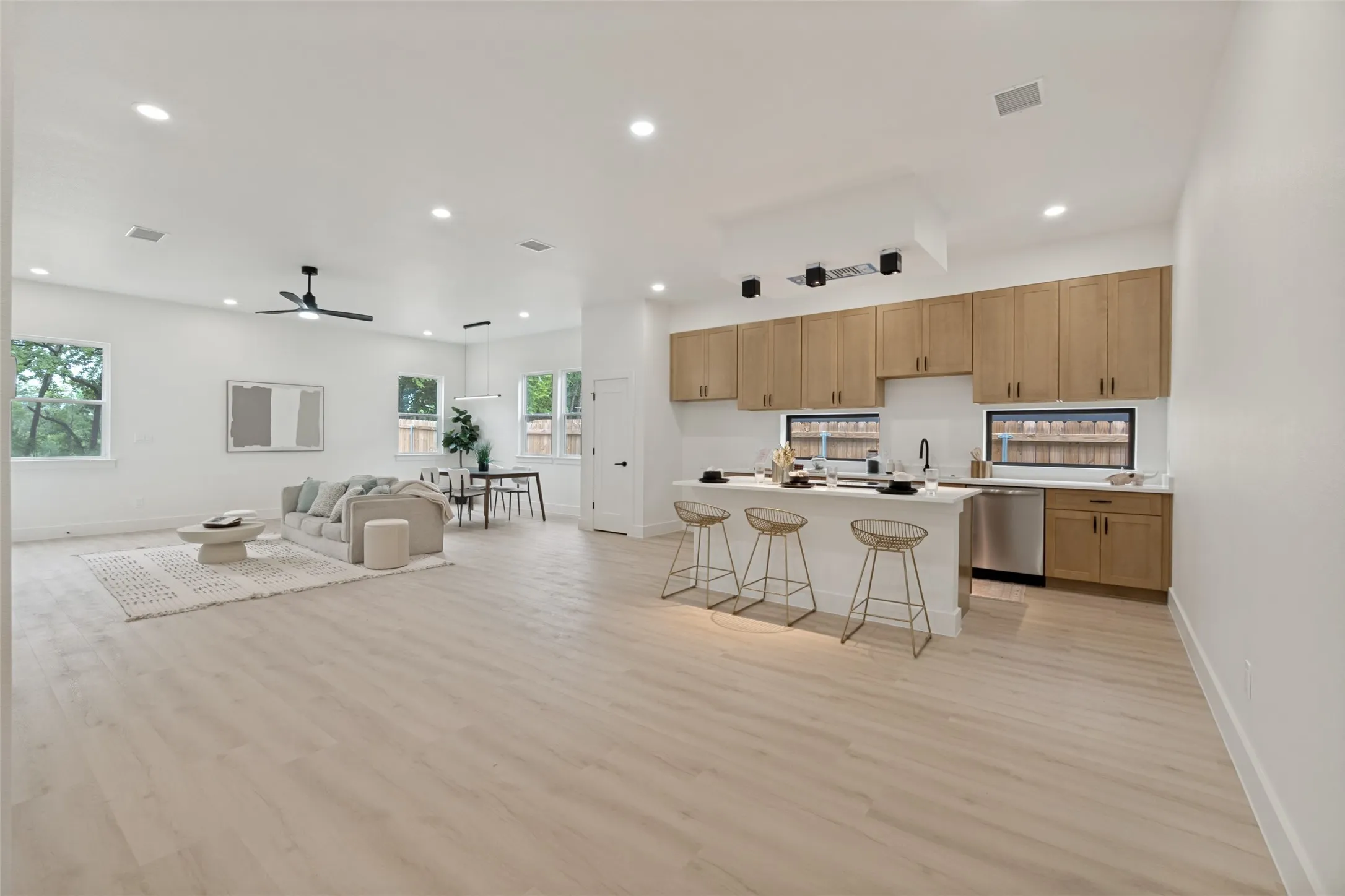 Open concept living area featuring light wood-finish flooring, recessed lighting, a modern kitchen with light wood cabinetry, white countertops, and stainless steel appliances