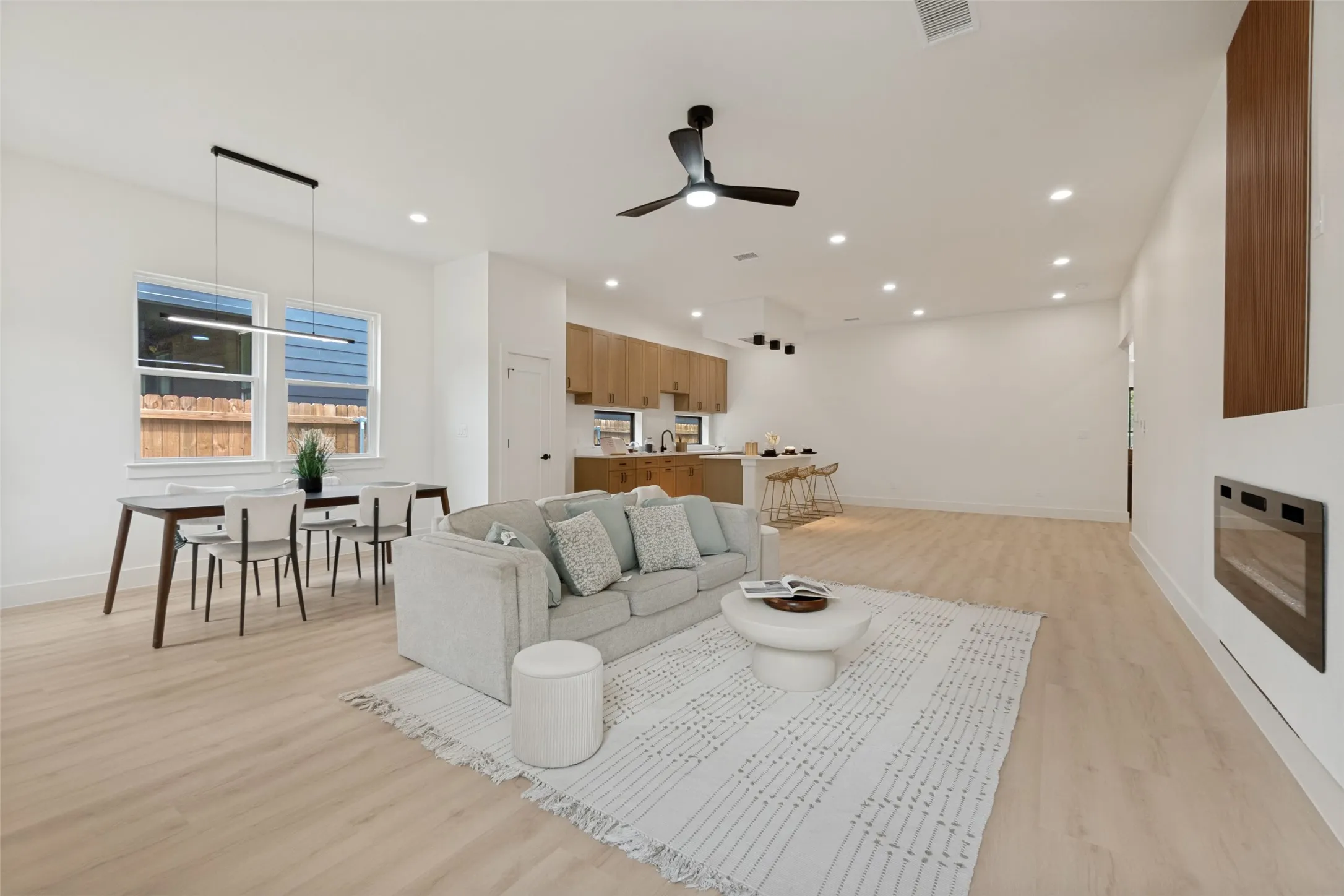 Spacious open-concept living area featuring light wood-finish flooring, recessed lighting, and a modern ceiling fan