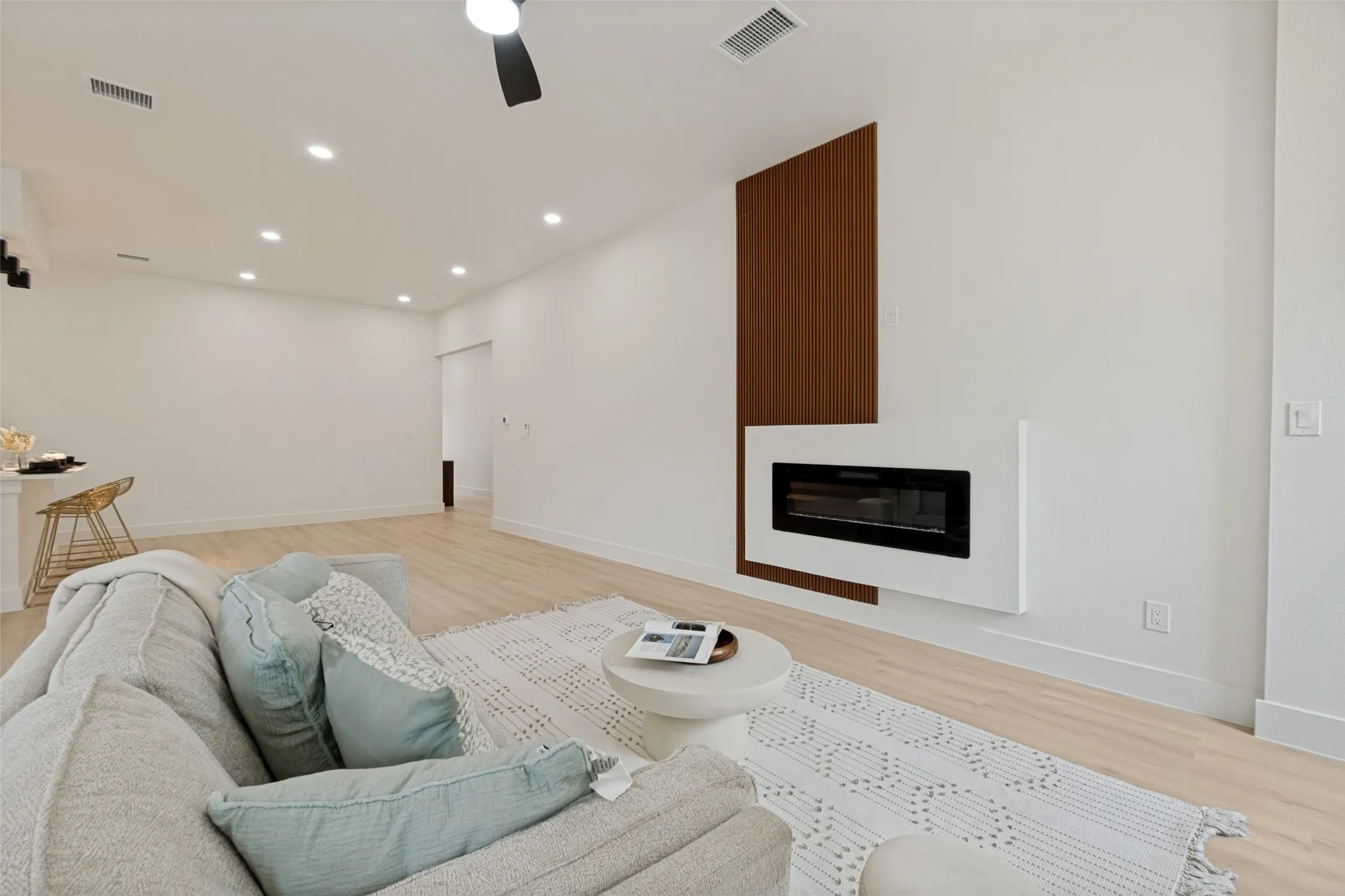 Contemporary living area featuring wood-finish flooring and a minimalist electric fireplace with a wood panel accent