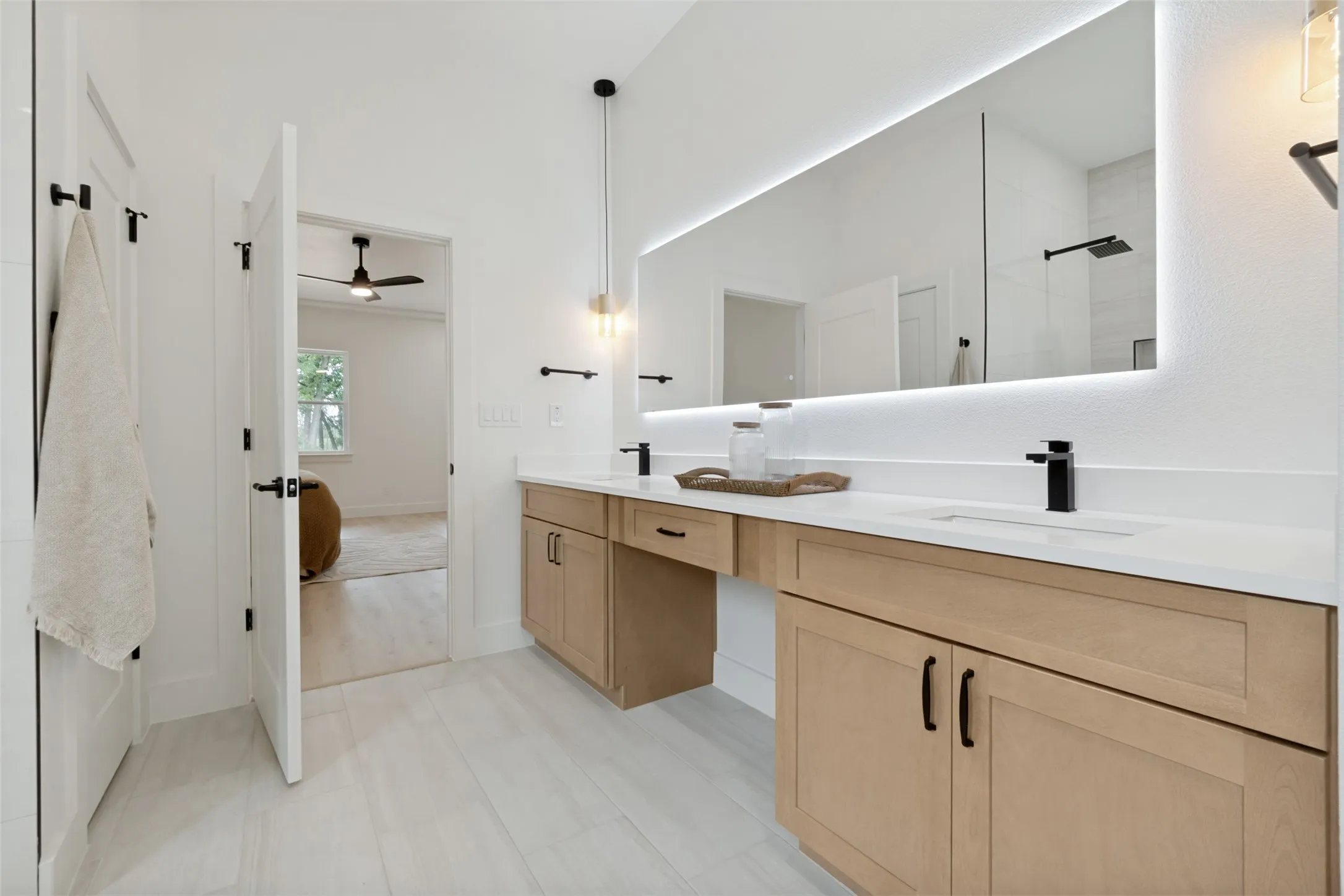 Contemporary bathroom featuring a double vanity with light wood cabinetry, white countertops, and matte black fixtures