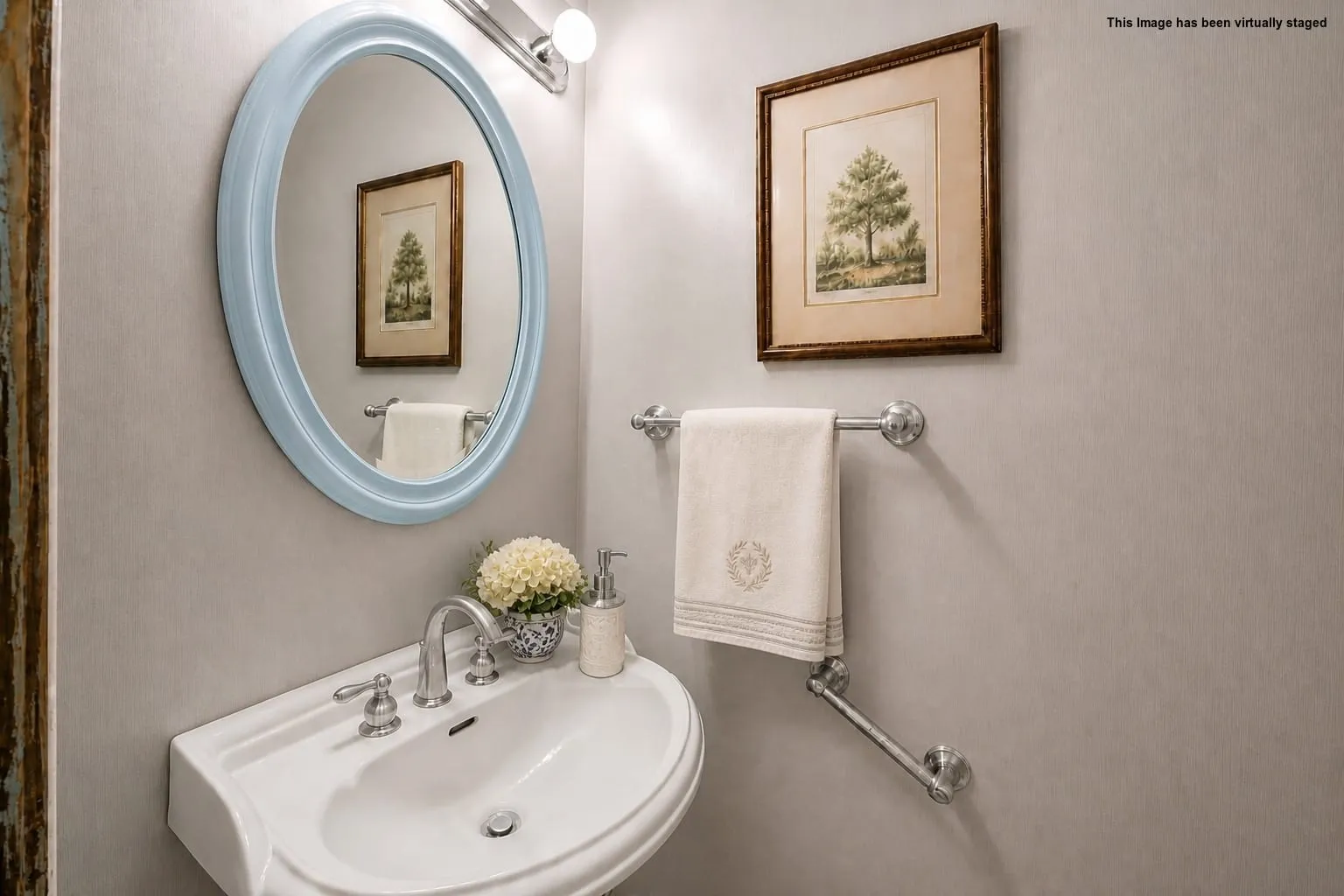 Wall-mounted porcelain sink with chrome fixtures, oval framed mirror, and a wall-mounted towel bar