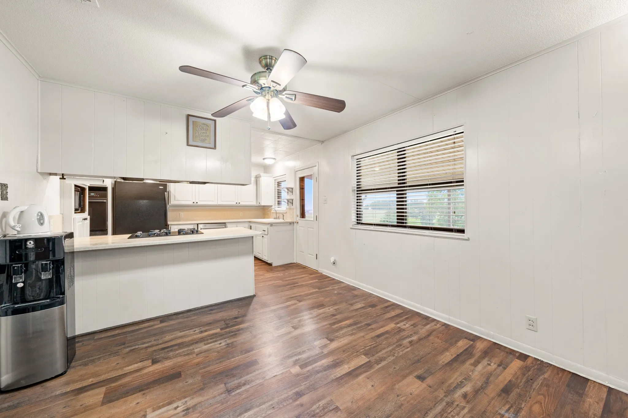 Wood-finish flooring, white panel walls, and a ceiling fan with light fixture