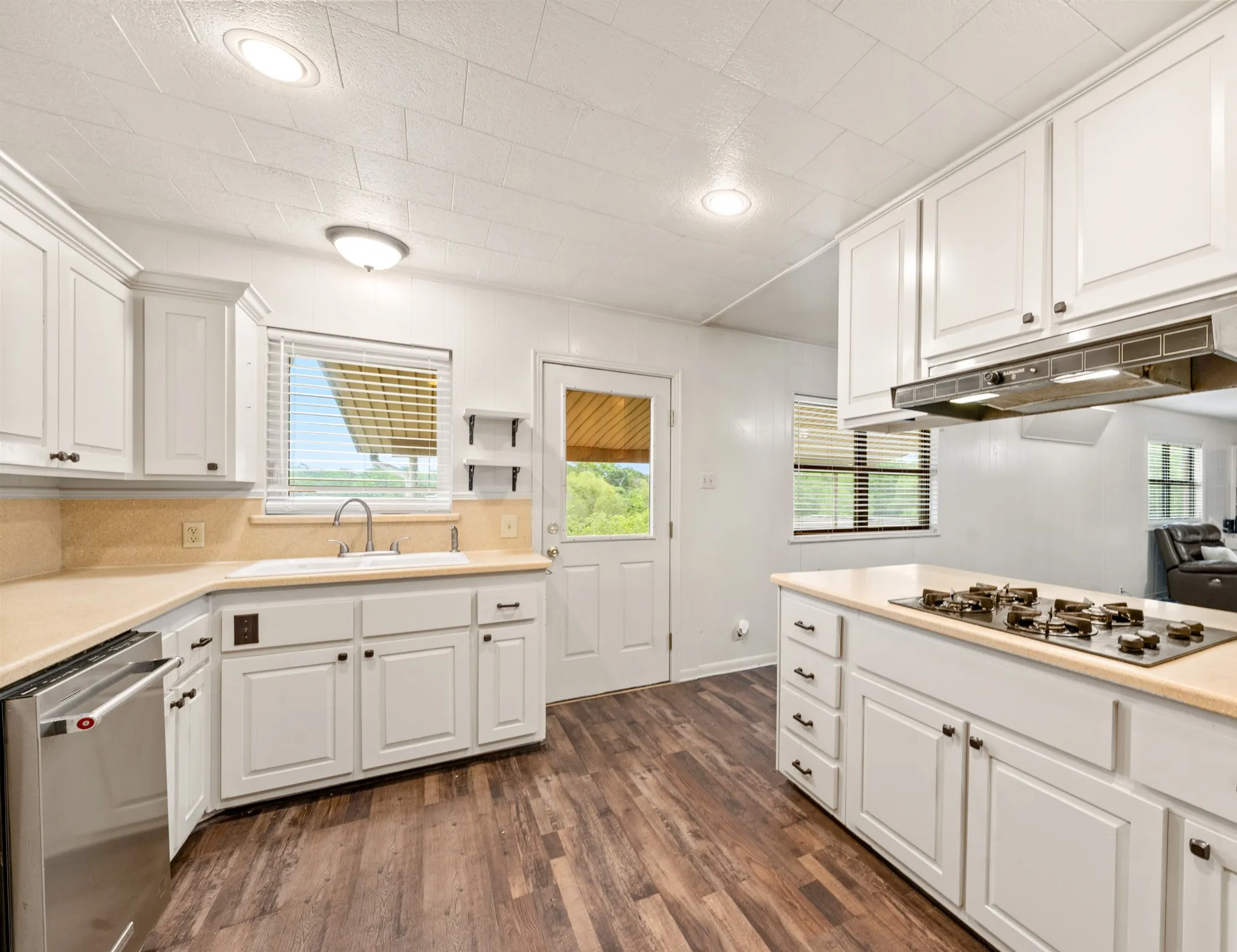 White cabinetry, wood-finish flooring, stainless steel dishwasher, built-in cooktop, and recessed lighting