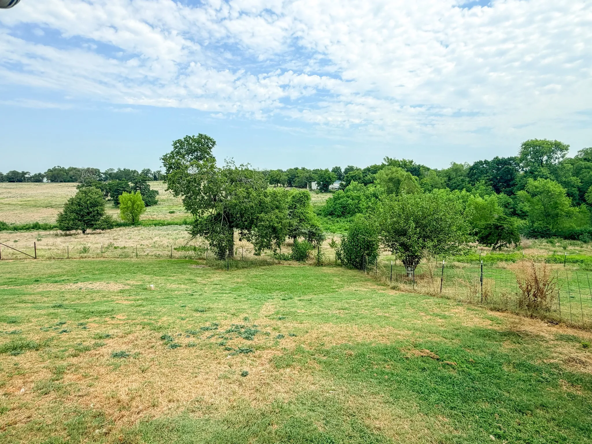 Expansive open land with mature trees and partial fencing