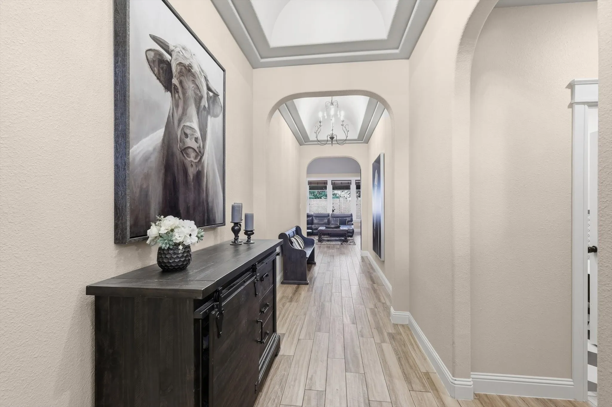 Arched entryways leading to an interior hallway with wood-finish flooring, tray ceiling, and crown molding