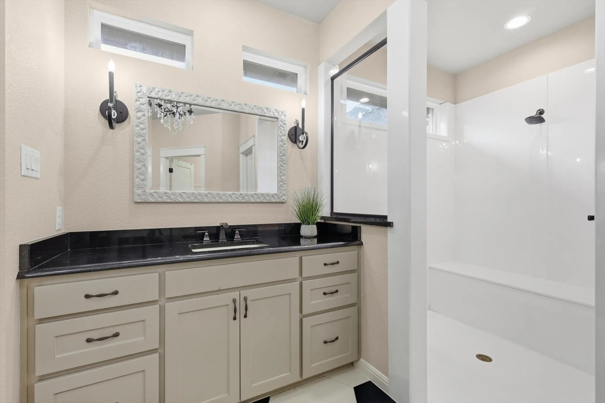 Bathroom featuring a single vanity with stone countertop, white cabinetry with dark hardware, and a walk-in shower with a built-in bench
