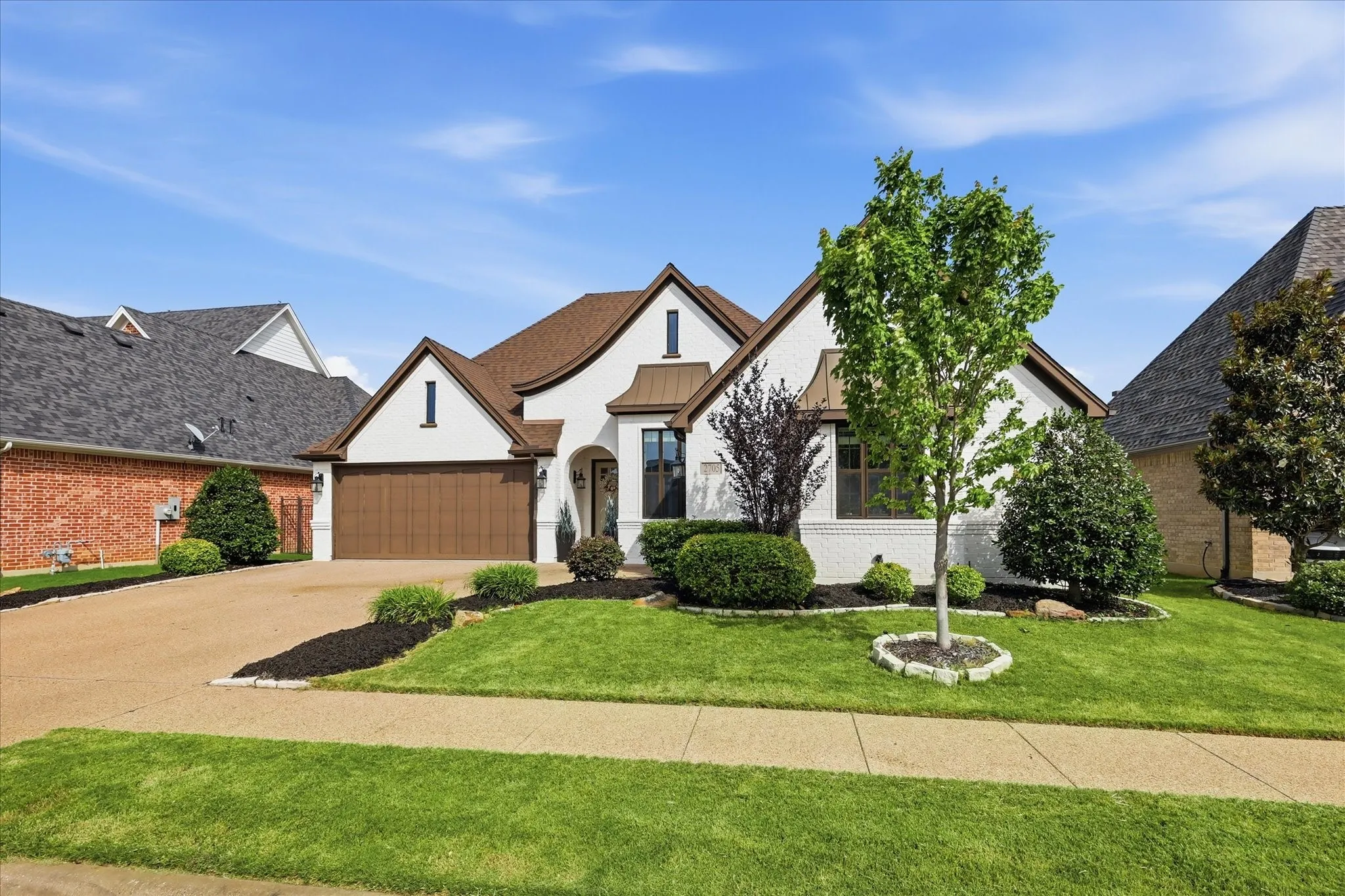 Exterior features include a white painted brick facade, brown garage door, arched entry, brown shingle roof, and a gravel driveway