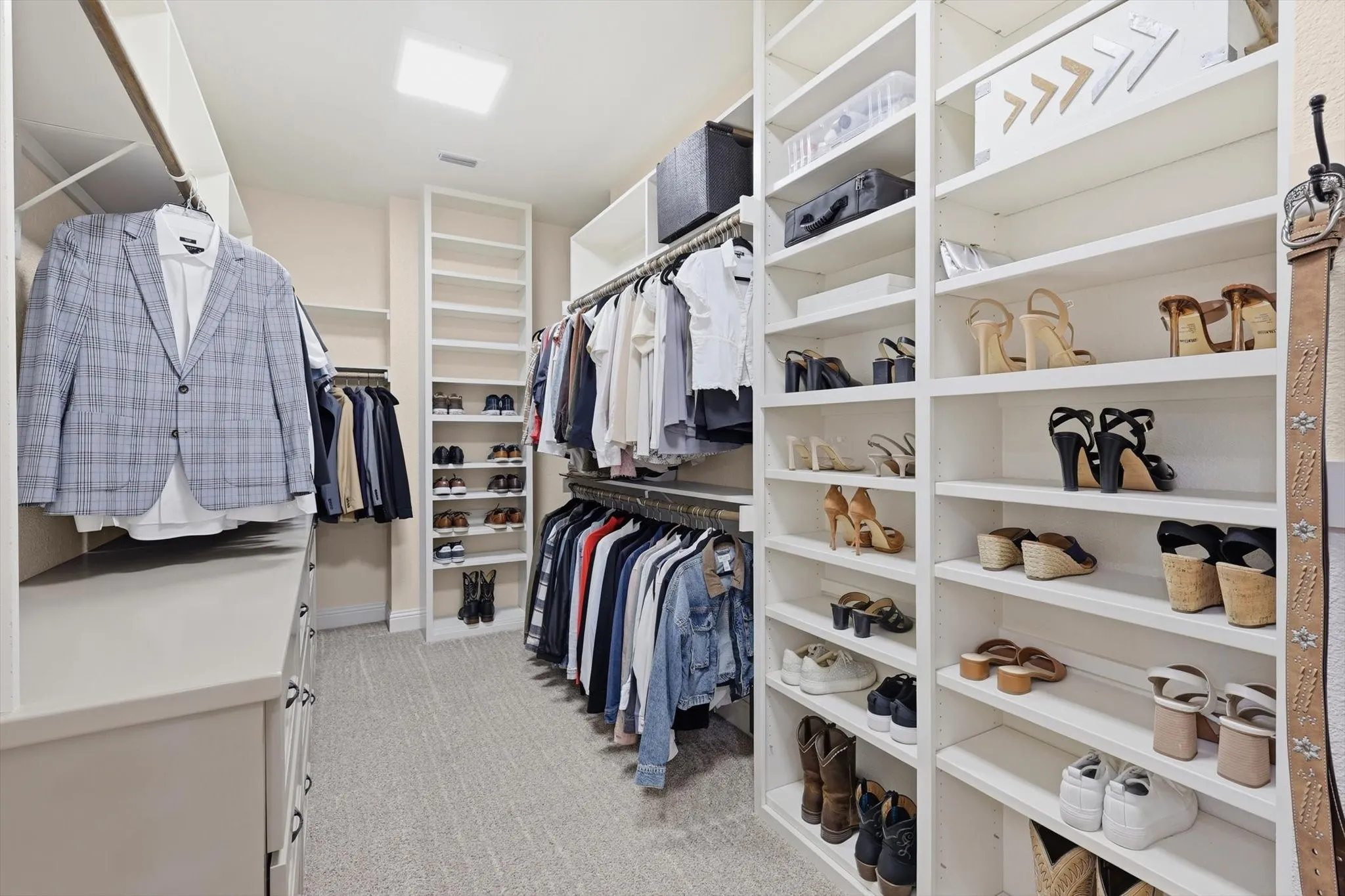 Spacious walk-in closet featuring extensive built-in shelving, multiple hanging rods, a central storage island, light-toned carpeting, and recessed ceiling lighting
