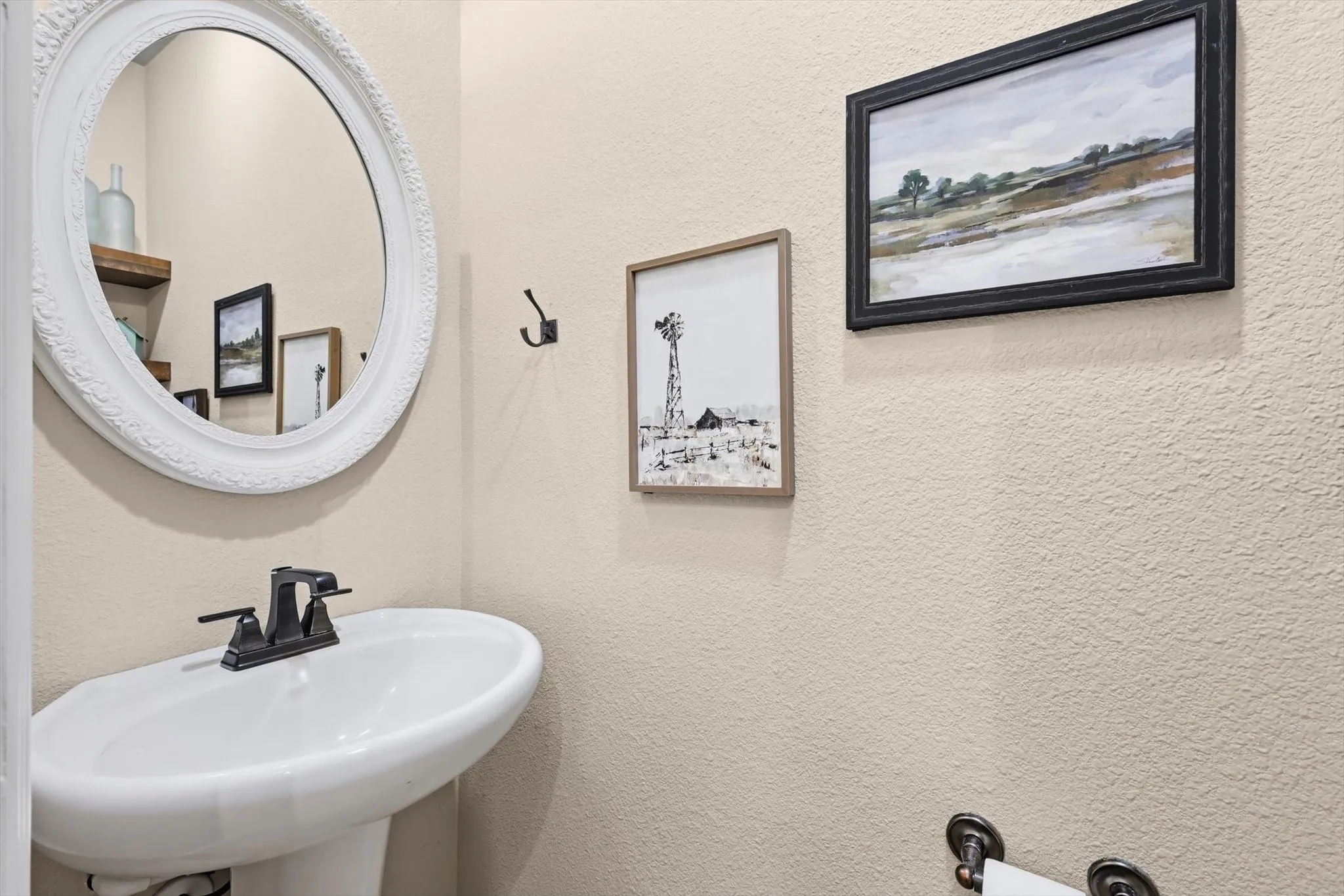 Pedestal sink with dark-finished faucet, complemented by a large white framed mirror
