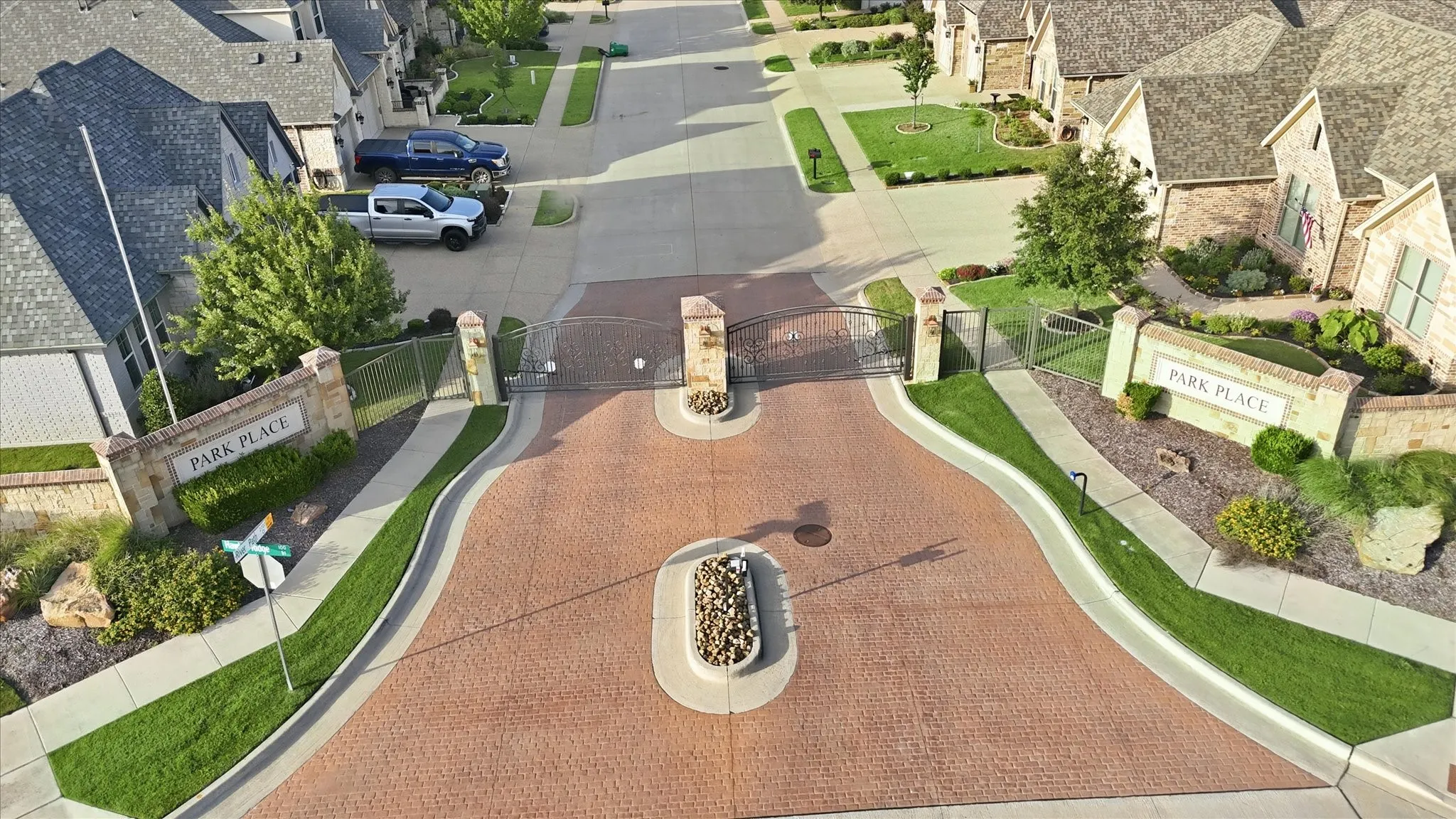 Gated community entry featuring brick pavers, stone pillars, and manicured landscaping