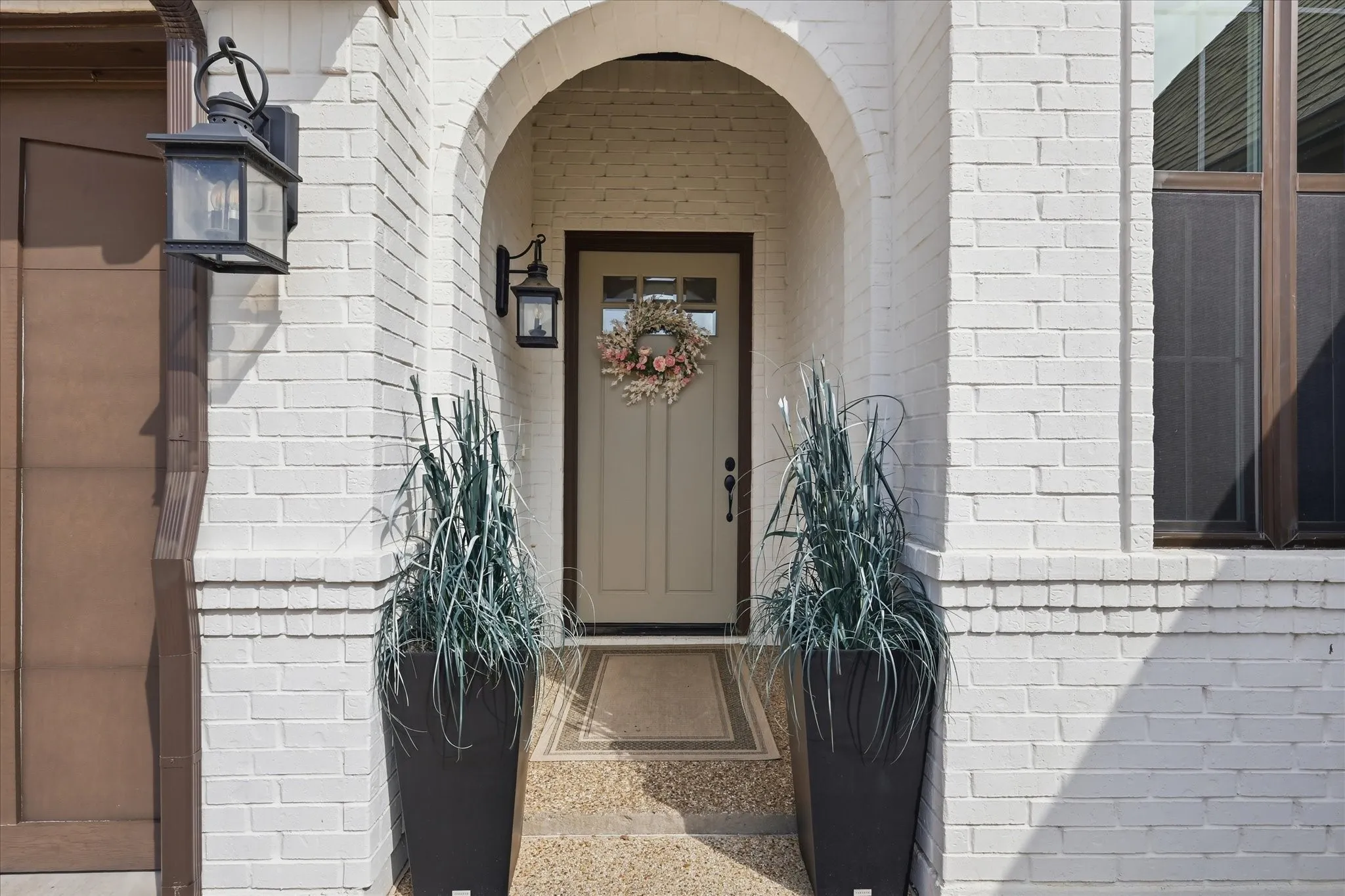 Arched entryway featuring painted white brick, a cream-colored entry door, and decorative sconce lighting
