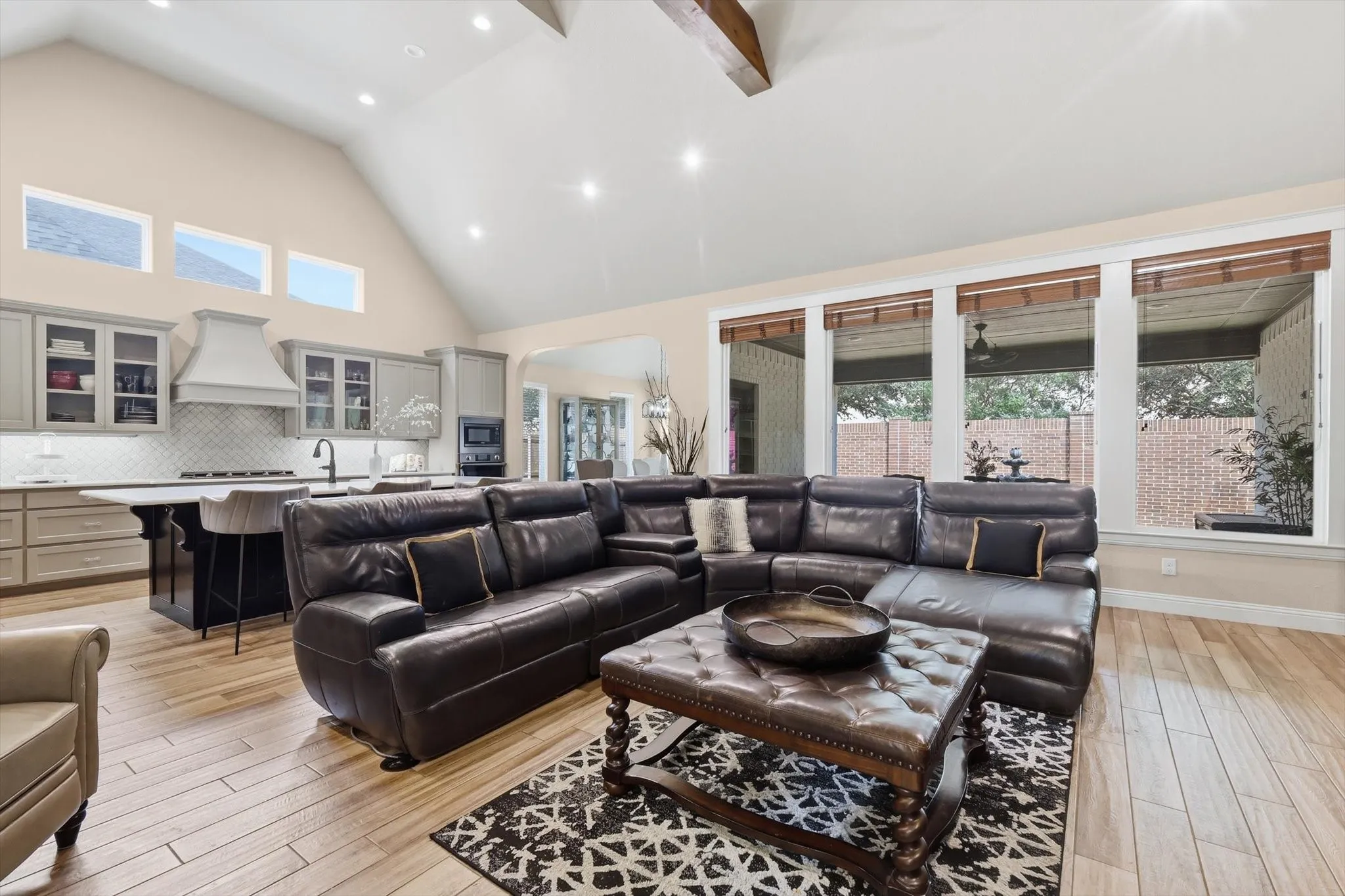 Spacious open-concept living area featuring a vaulted ceiling with exposed wood beams, recessed lighting, and light wood-finish flooring