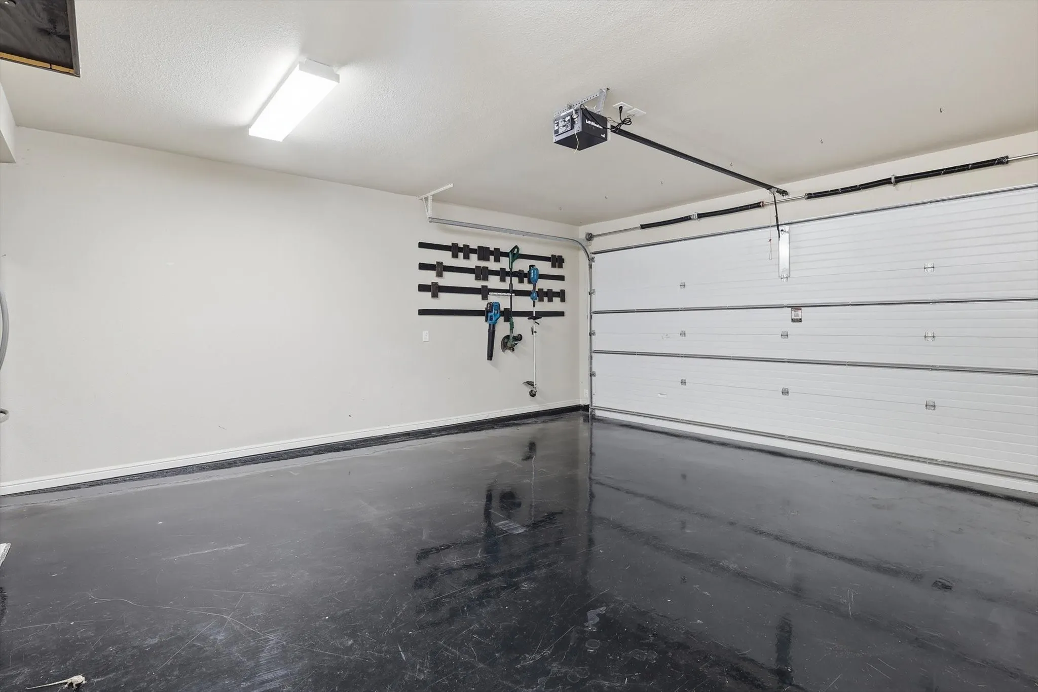 Spacious garage featuring a glossy black concrete floor, white insulated garage door, overhead fluorescent lighting, and wall-mounted storage racks