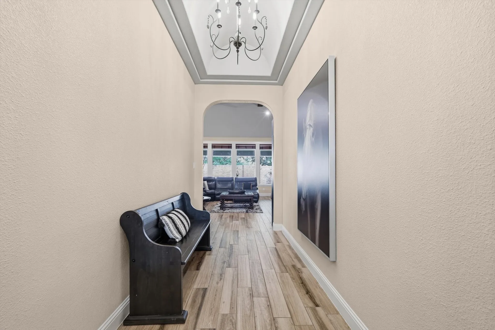 Hallway featuring wood-finish flooring, an arched entryway, a tray ceiling with crown molding, and a decorative chandelier
