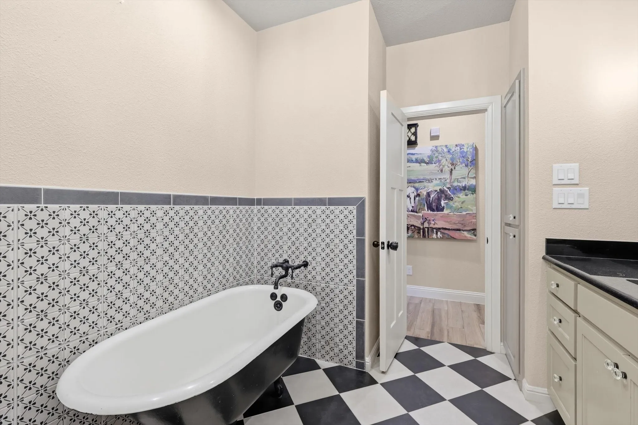 Freestanding clawfoot tub with matte black hardware, checkerboard tile flooring, and patterned wainscoting