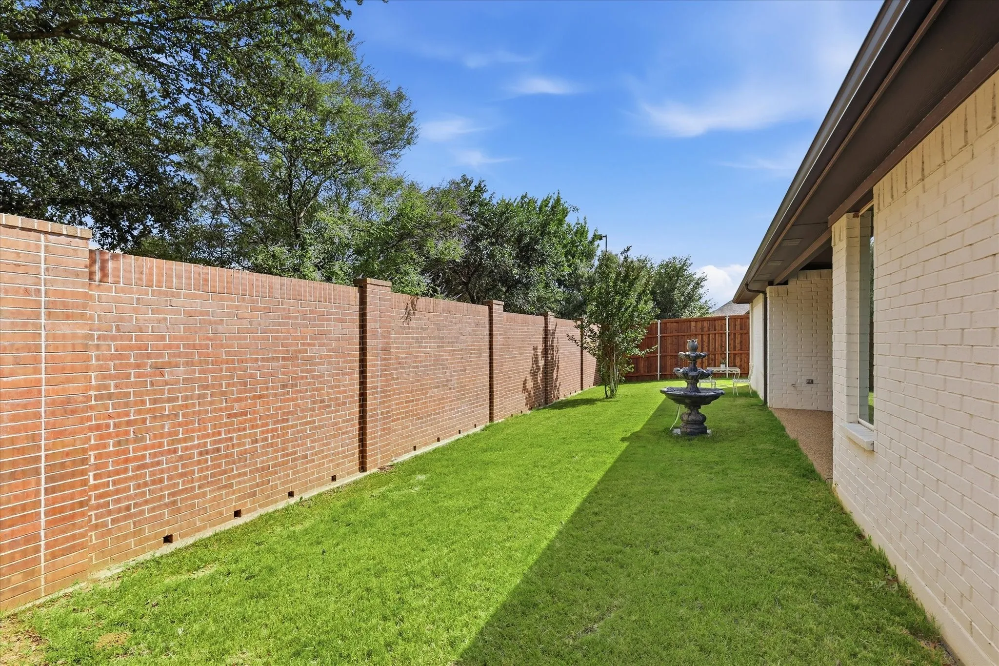 Side yard featuring a brick privacy wall, green lawn, and a decorative tiered fountain
