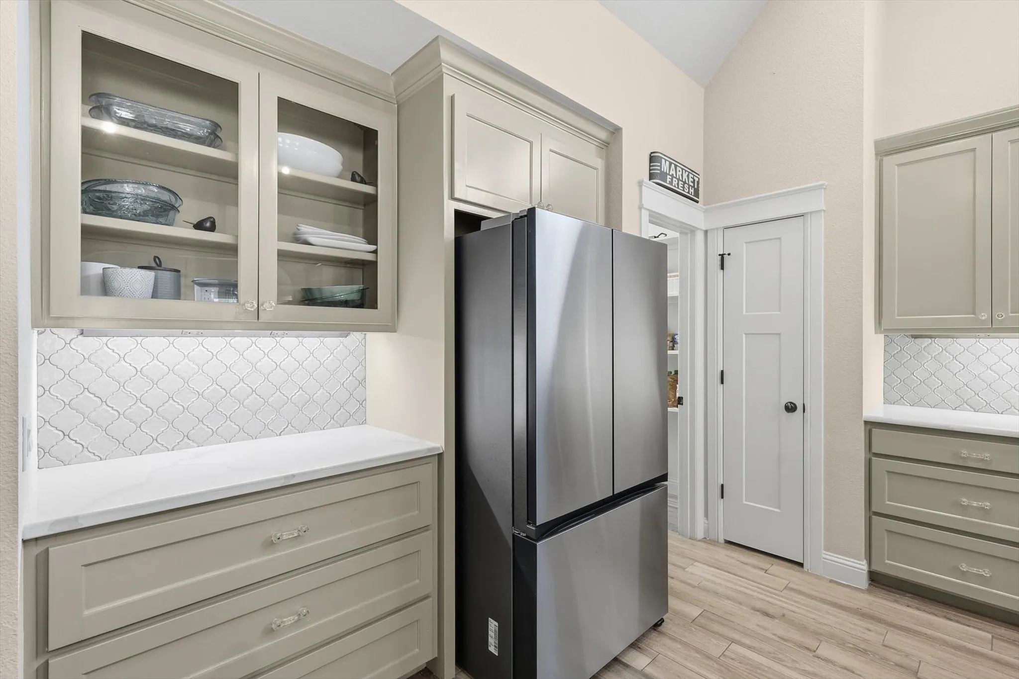 Kitchen featuring wood-finish flooring, light-colored cabinetry, patterned tile backsplash, and stainless steel refrigerator