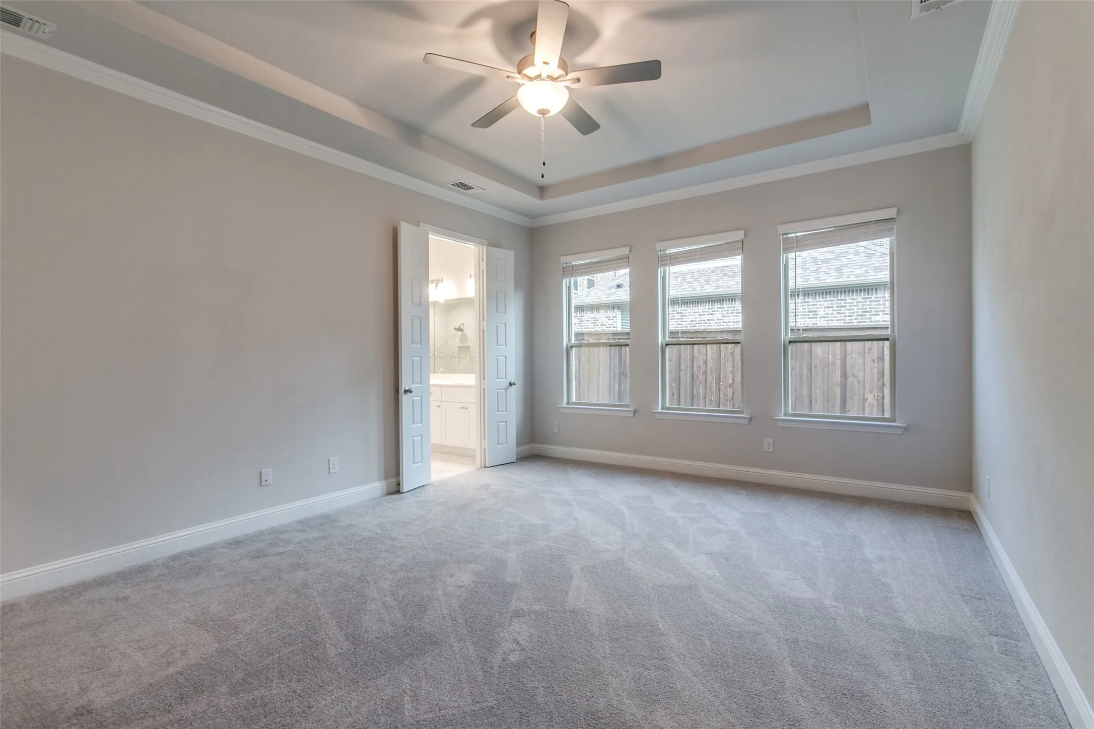 Spacious room featuring light gray carpeting, neutral wall paint, and a tray ceiling with a ceiling fan