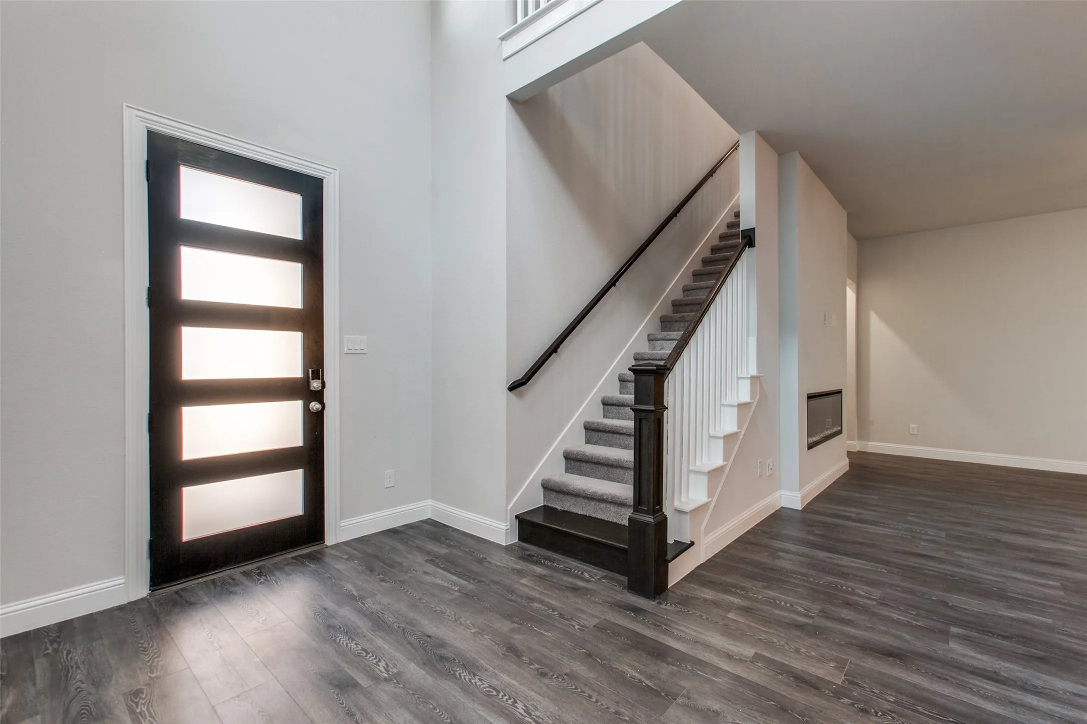 Entryway featuring a modern front door with frosted glass panels, wood-finish flooring, a carpeted staircase with dark wood newel post and handrail, and an integrated fireplace