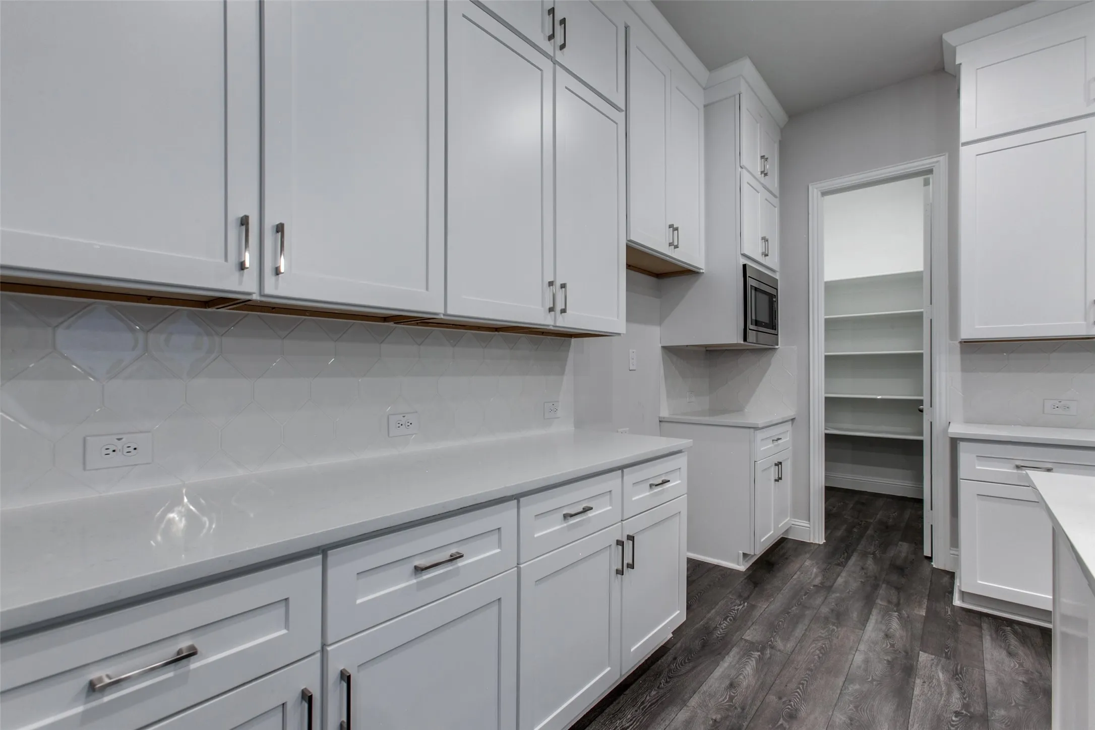 Kitchen featuring white shaker cabinetry, light-toned countertops, a patterned tile backsplash, dark wood-finish flooring, and a built-in microwave