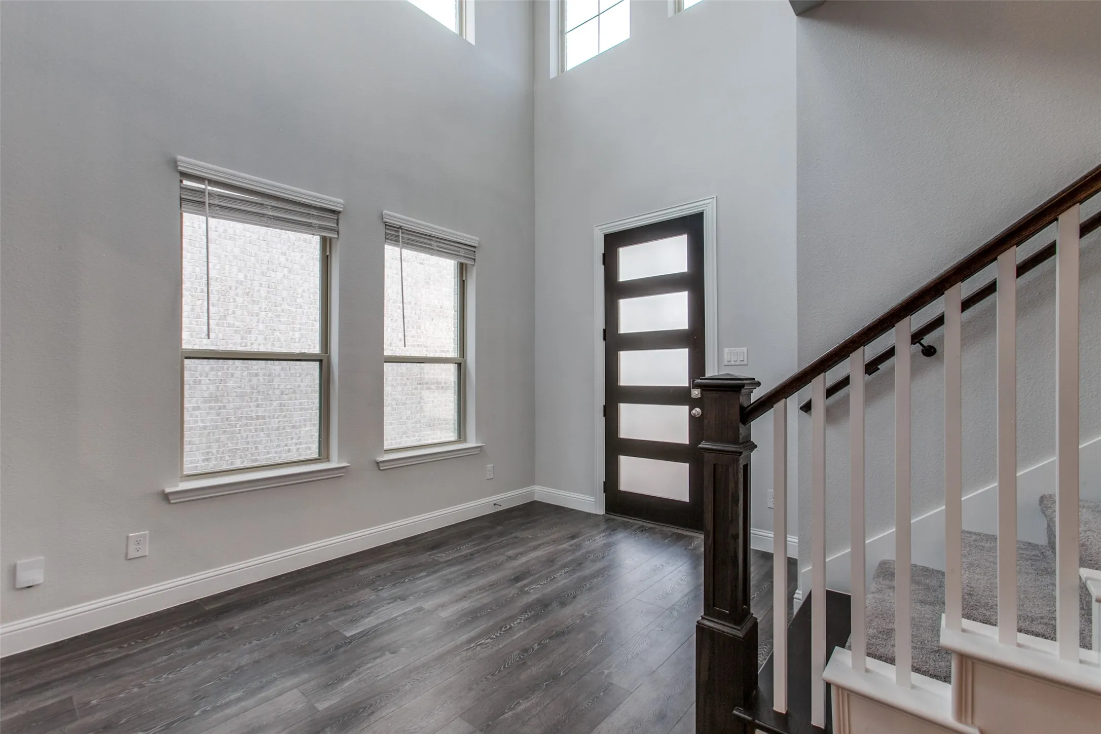Two-story entry foyer featuring wood-finish flooring, a contemporary front door with frosted glass panels, and a staircase with white balusters and a dark wood handrail