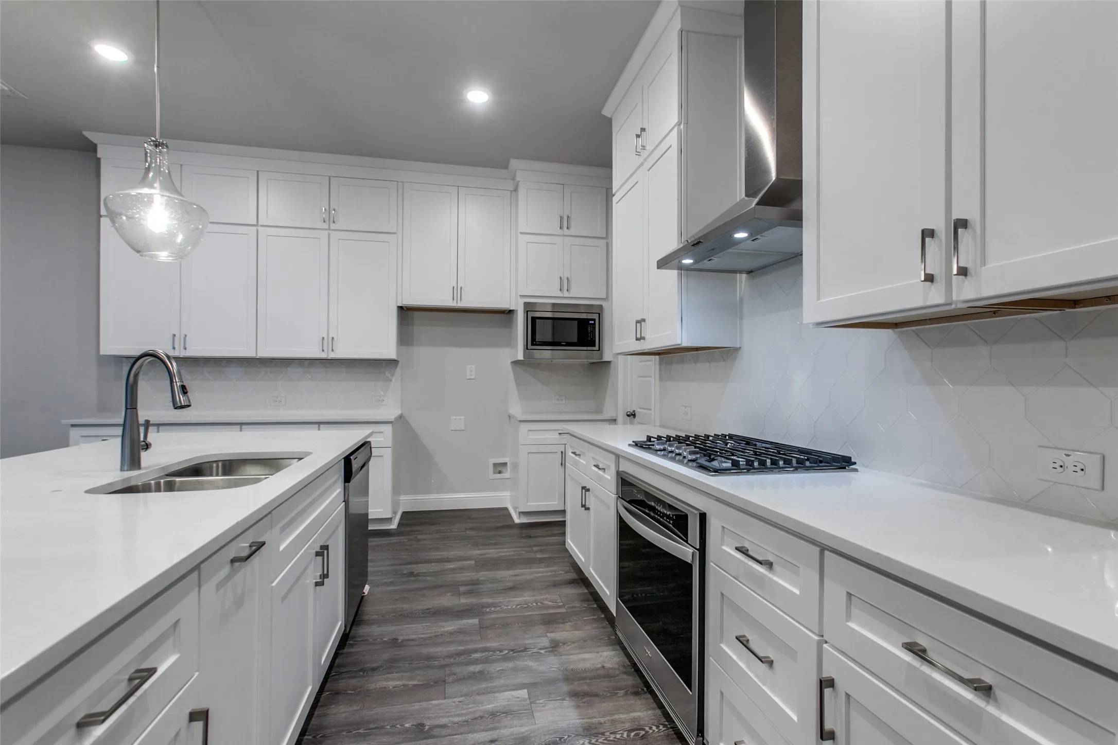 Kitchen featuring white shaker cabinetry, light-toned countertops, stainless steel appliances, a tile backsplash, and wood-finish flooring