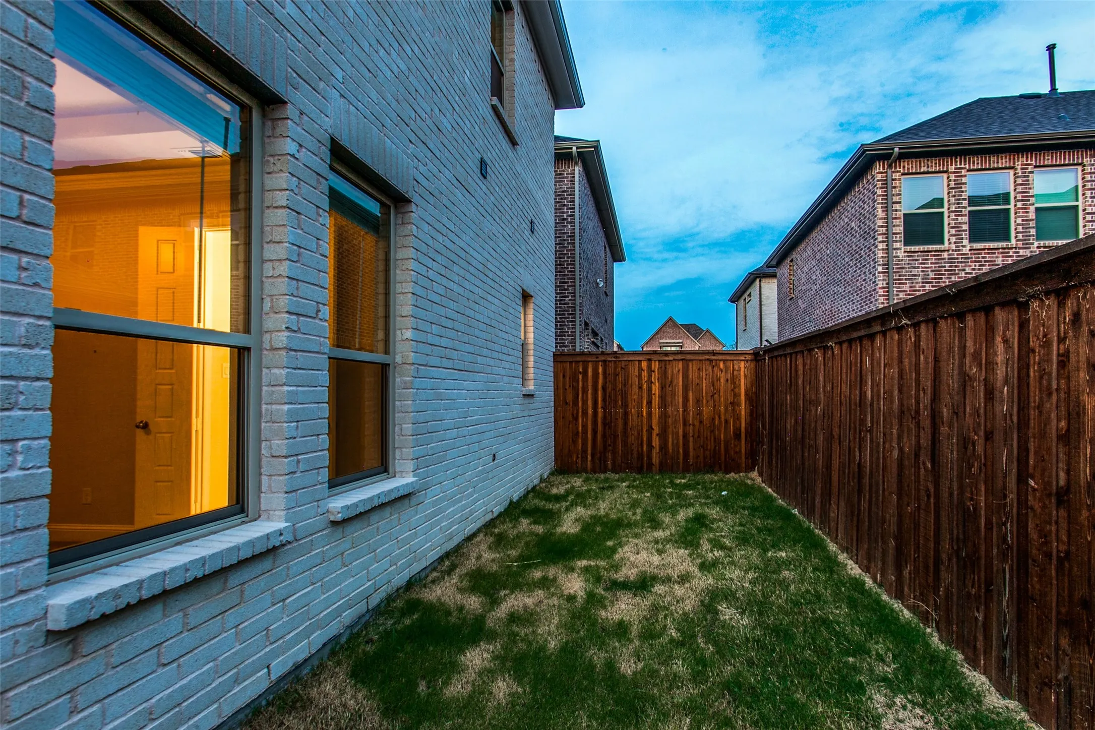 Private backyard featuring a new wood fence, a manicured lawn, and brick exterior walls