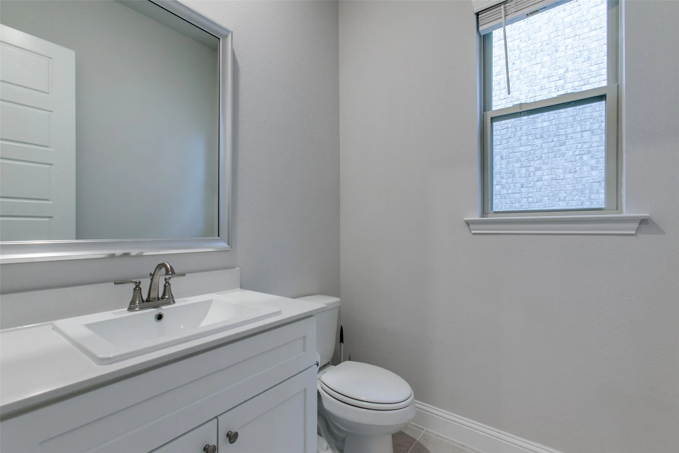 Powder room featuring a white single-sink vanity with a light countertop, a framed mirror, and a toilet